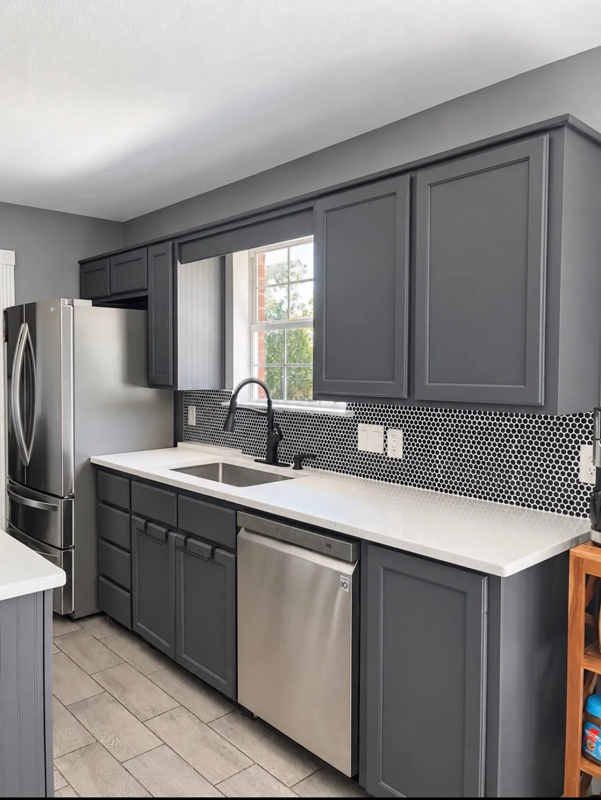 Contemporary kitchen featuring dark gray shaker cabinetry, stainless steel appliances, a white solid surface countertop, and a black penny tile backsplash