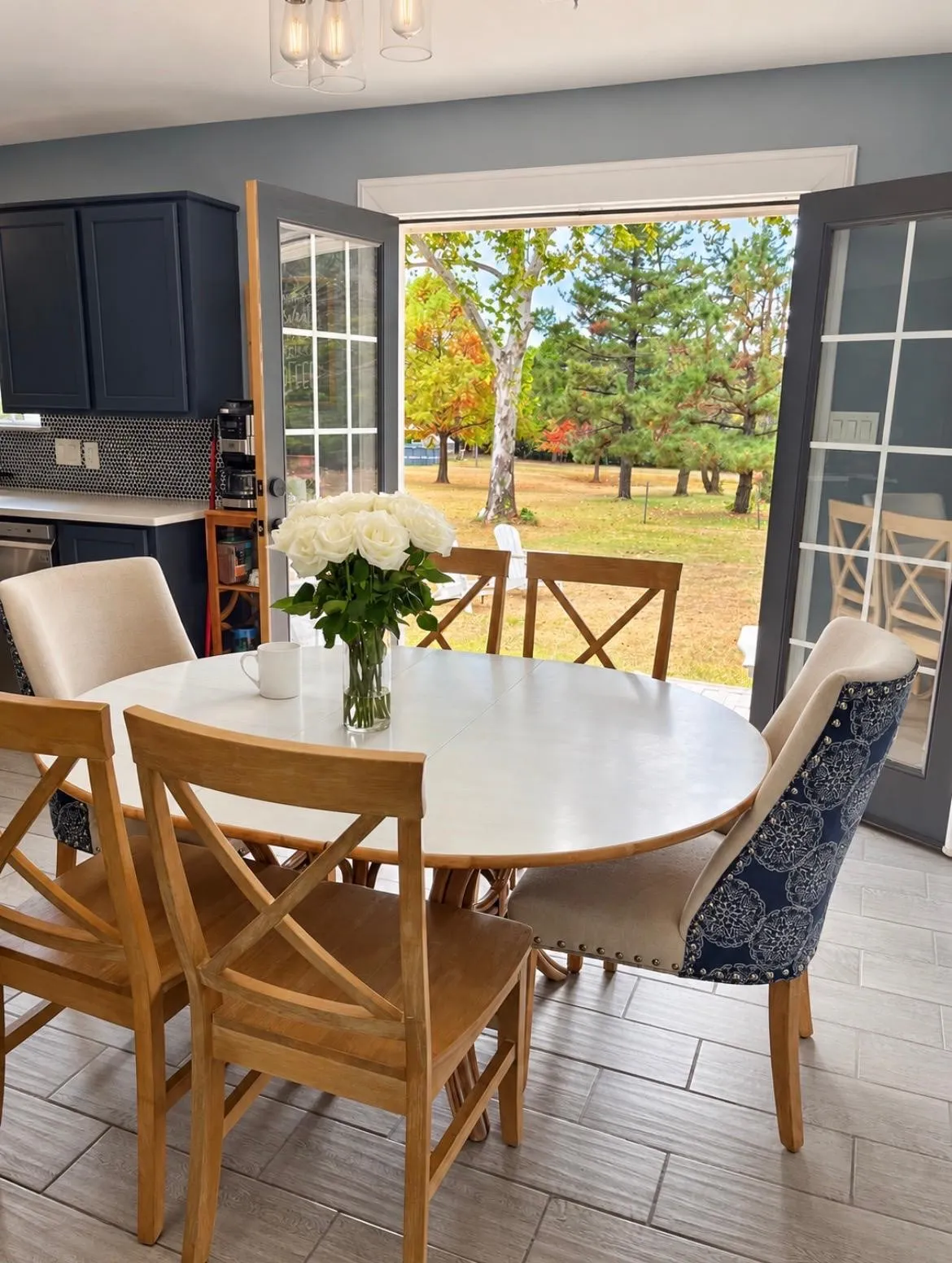 French doors opening to a lush backyard, dark cabinetry with tile backsplash, light wood-finish flooring, and a modern ceiling light fixture