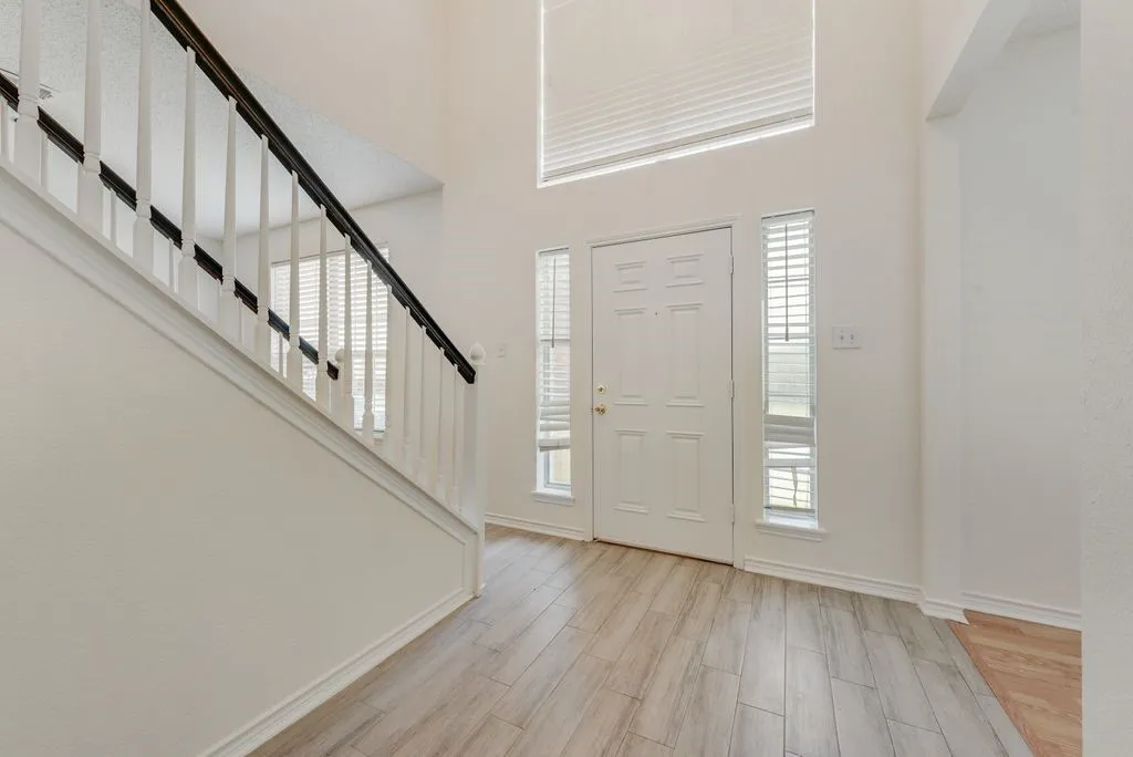 Two-story entryway featuring wood-finish flooring, a white paneled front door, and a staircase with white spindles and a dark handrail