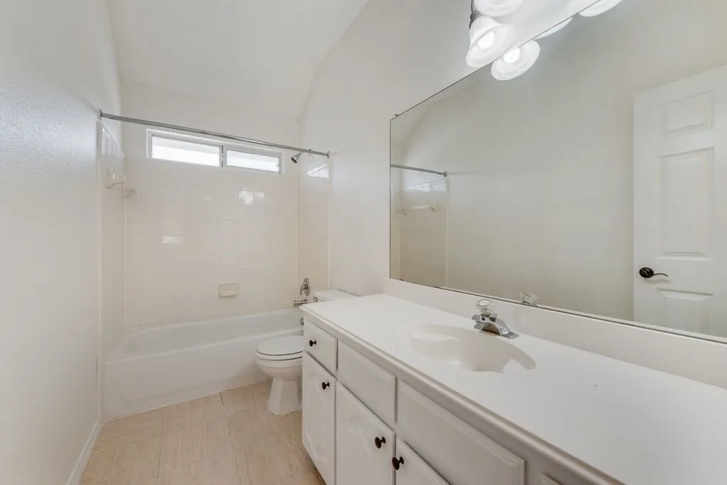 Bathroom featuring a single vanity with an integrated sink, a large wall-mounted mirror, a tub-shower combination, an overhead window, and tile flooring