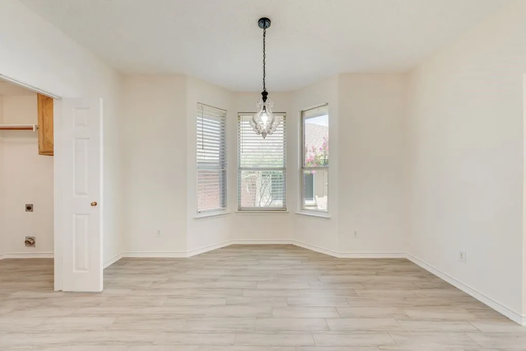 Bright interior space featuring a multi-paned bay window with blinds, wood-finish flooring, a contemporary chandelier, and a utility closet with shelving and cabinetry