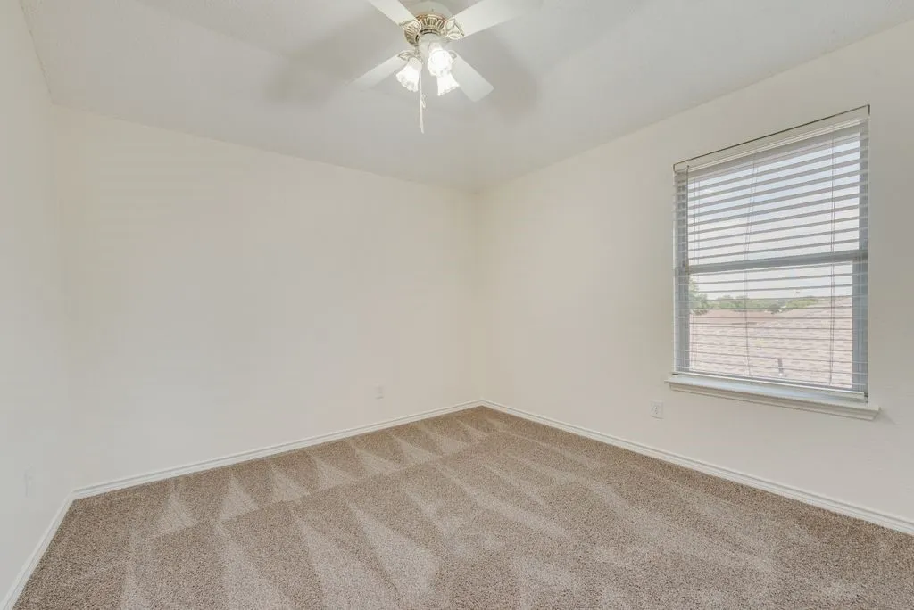Carpeted room featuring a ceiling fan with light fixture and a window with horizontal blinds