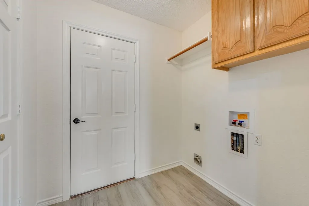 Laundry area featuring wood-finish flooring, white walls, and a white paneled door with dark hardware