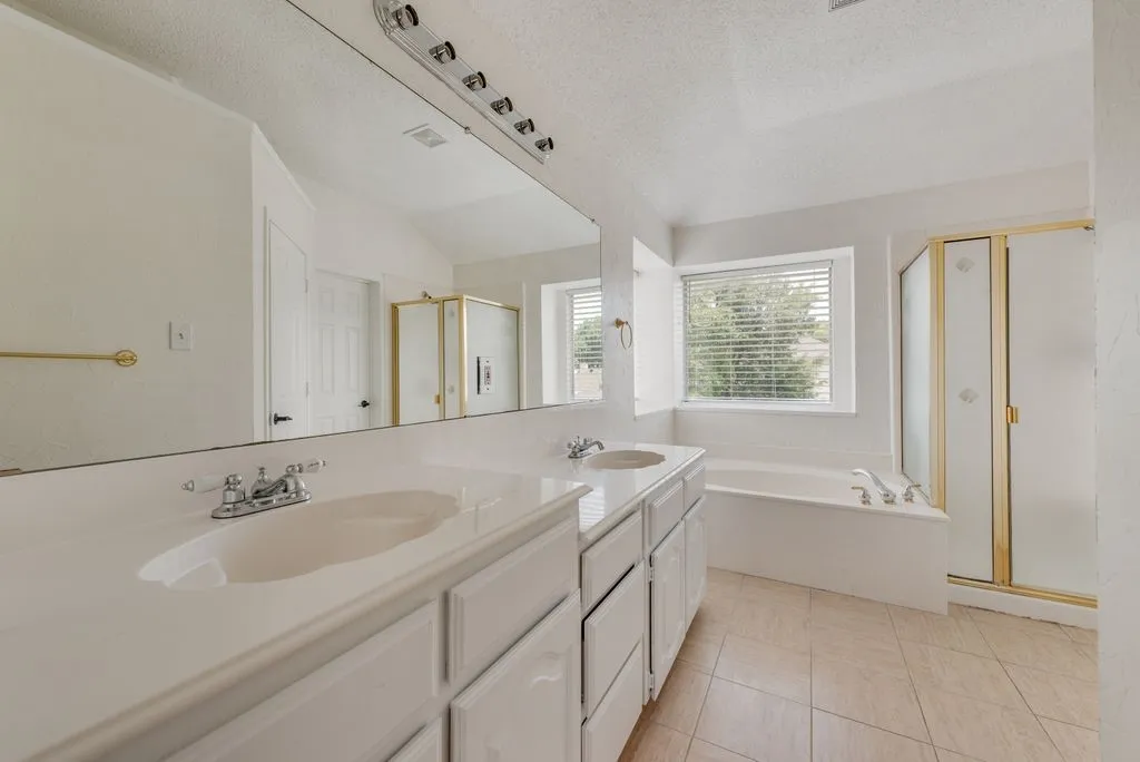 Bathroom featuring a dual vanity with integrated sinks, a built-in bathtub, and a separate shower enclosure with gold-toned framing