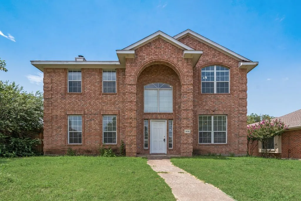 Two-story brick exterior featuring an arched entryway, multiple double-hung windows, and a paved walkway leading to the front door