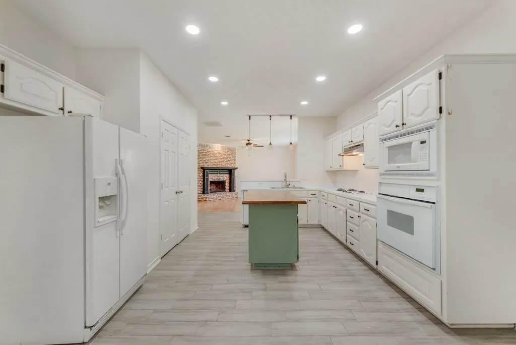Galley kitchen featuring wood-finish flooring, white cabinetry, integrated oven and microwave, a center island with a wood countertop, and recessed lighting