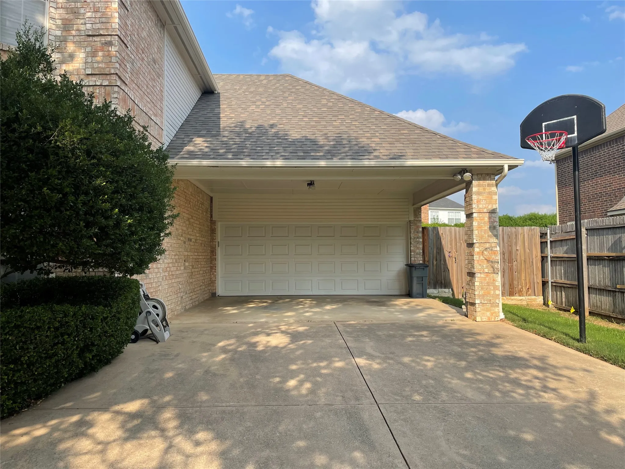 Attached two-car garage with a covered carport featuring a brick column and concrete driveway