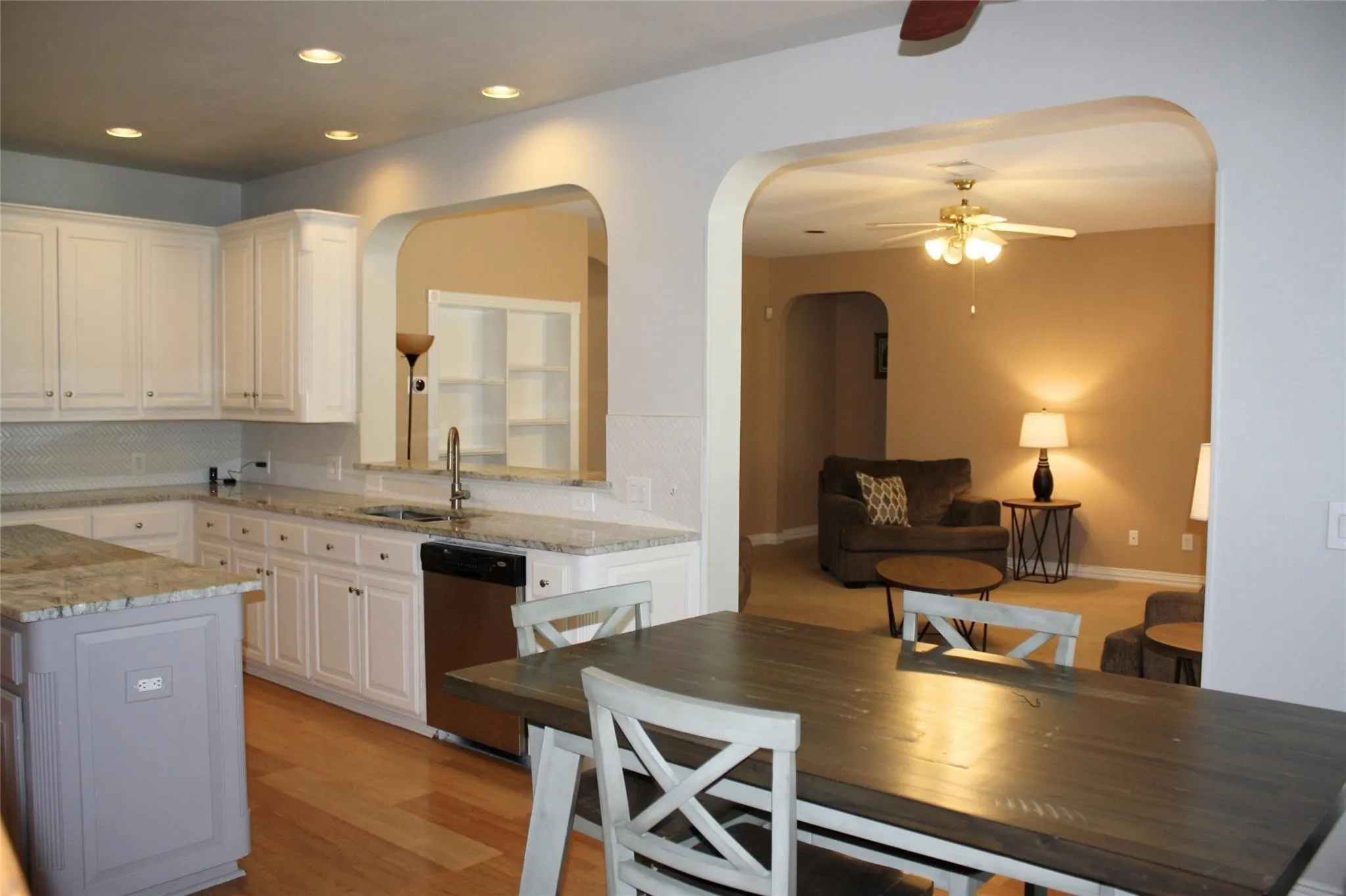 White cabinetry with granite countertops, stainless steel dishwasher, and hardwood-finish flooring