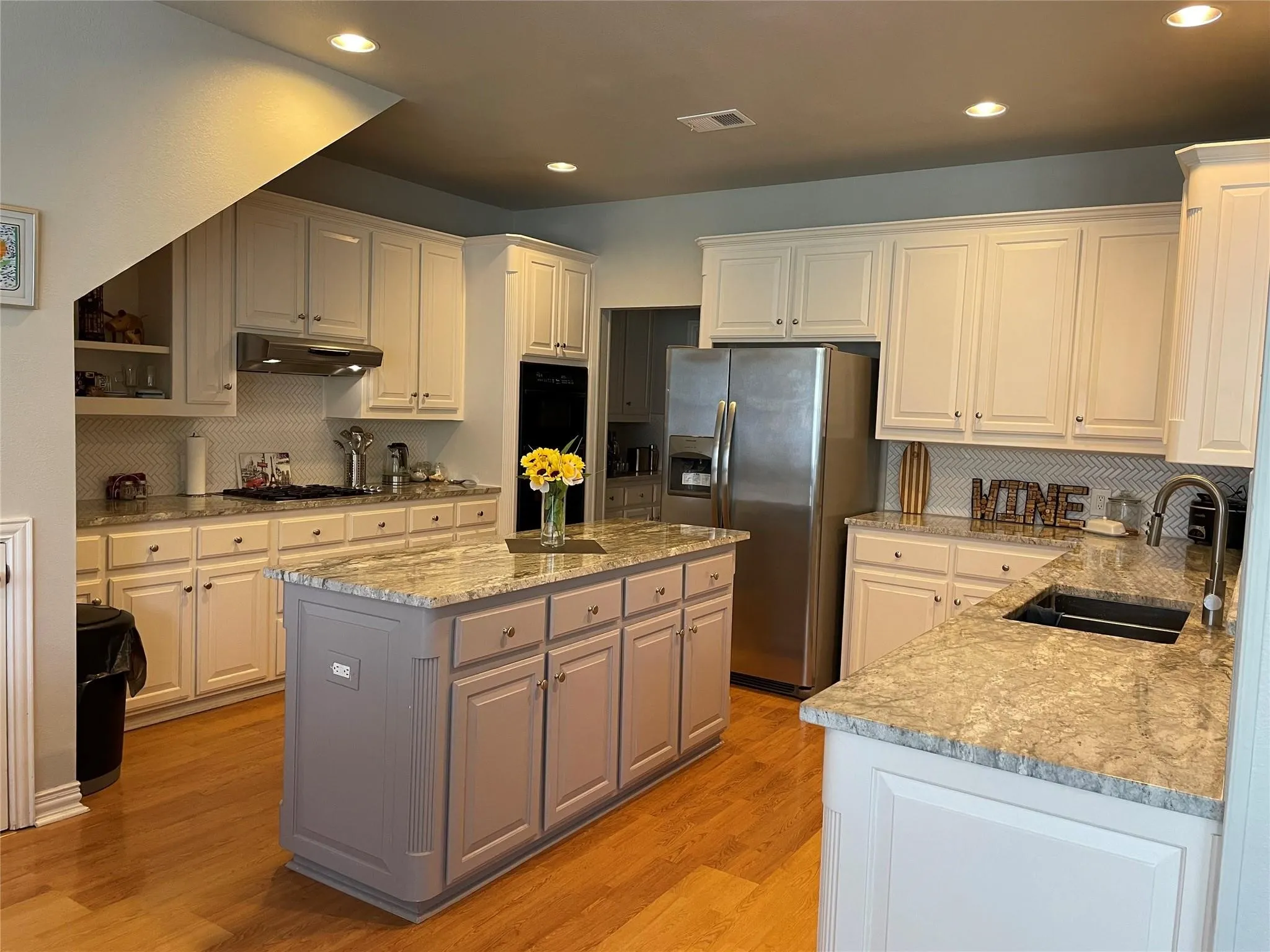 Kitchen featuring wood-finish flooring, recessed lighting, white cabinetry, a central island with a contrasting base, and light-toned countertops