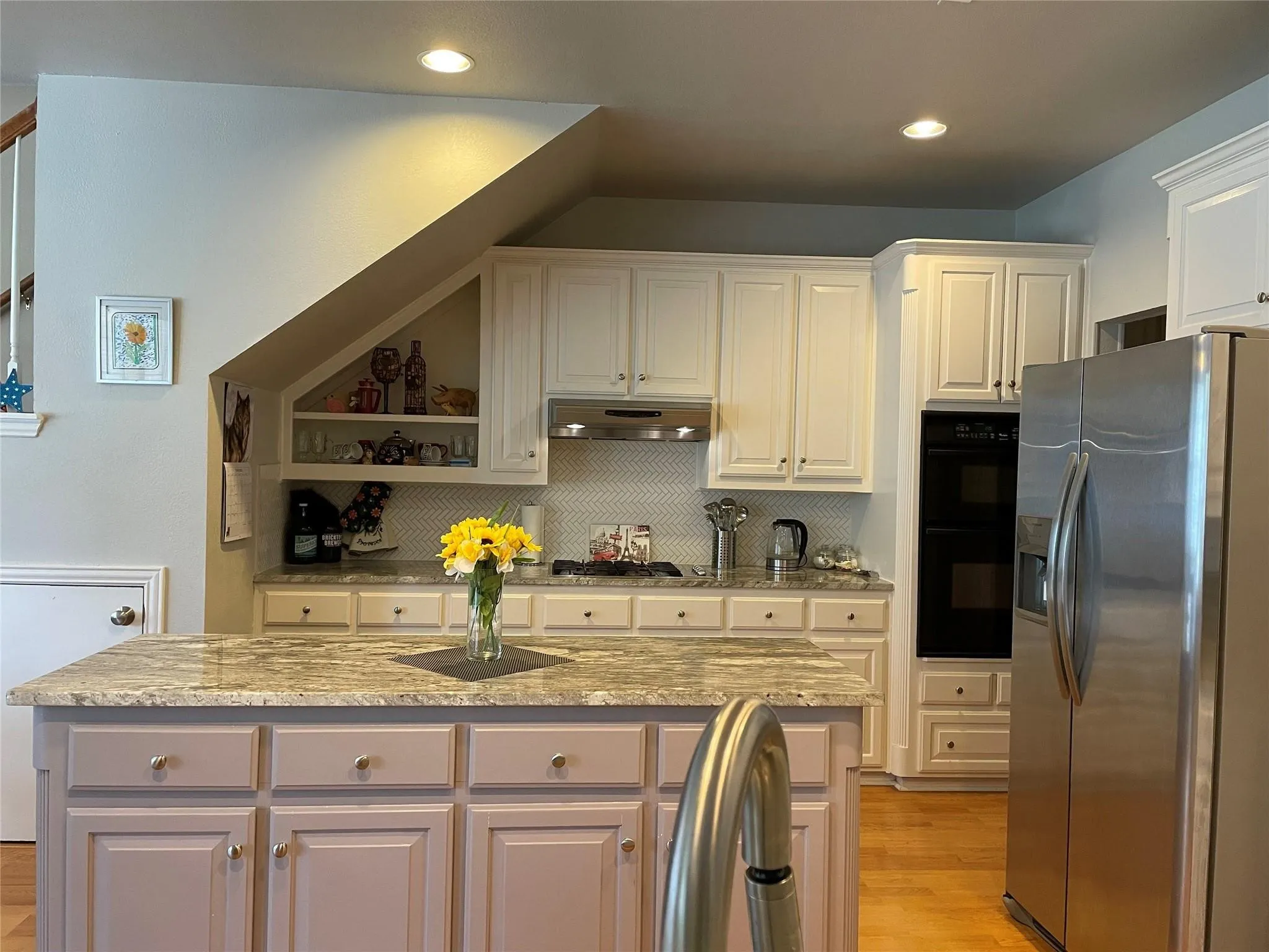 Kitchen featuring a central island with a stone countertop, built-in double oven, and stainless steel refrigerator