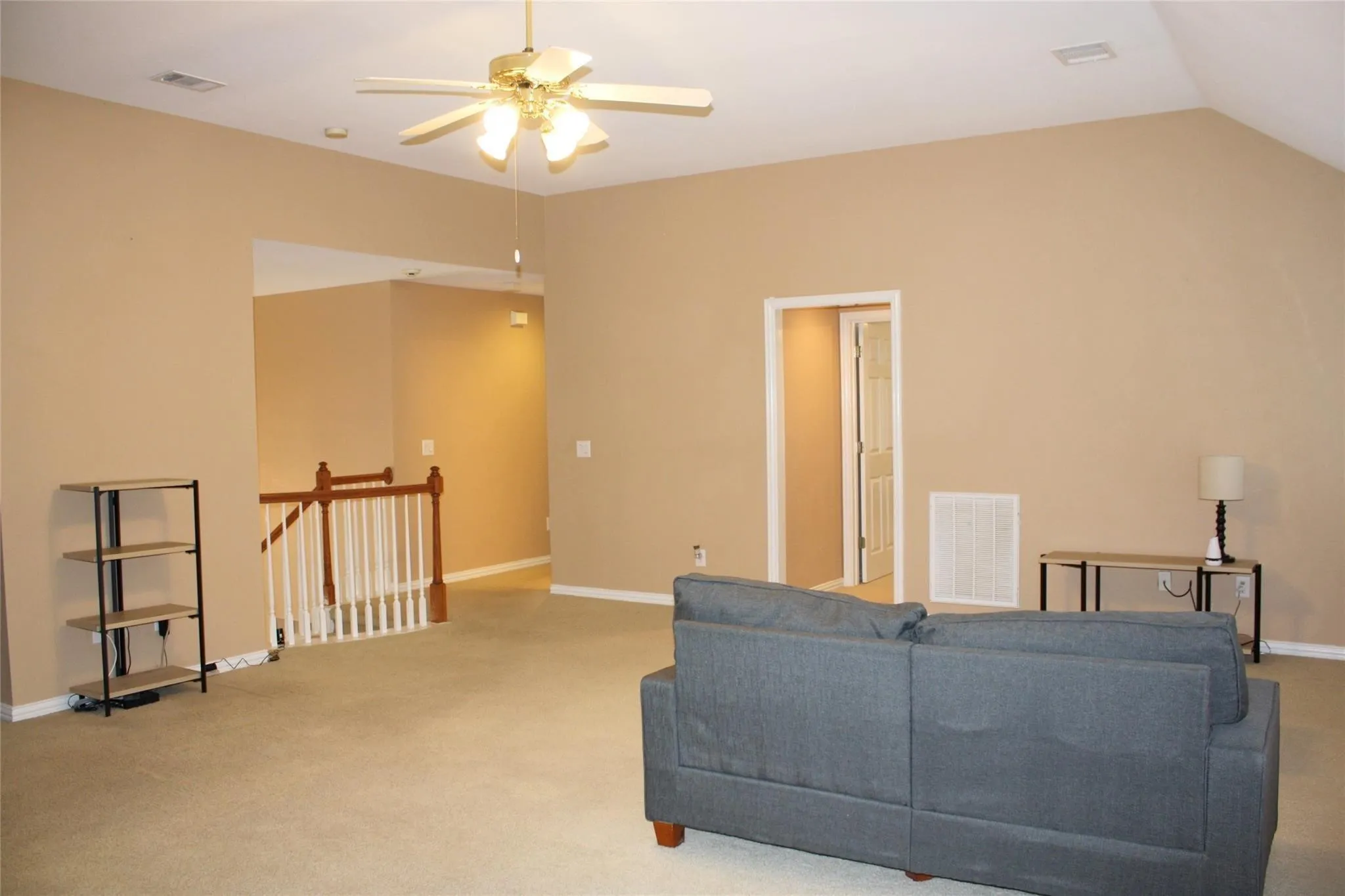 Carpeted living area with vaulted ceiling, ceiling fan, and staircase with wood railing and white balusters