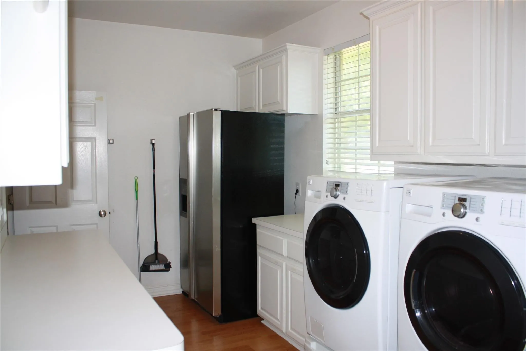 White paneled cabinetry, wood-finish flooring, white countertops, and window with blinds