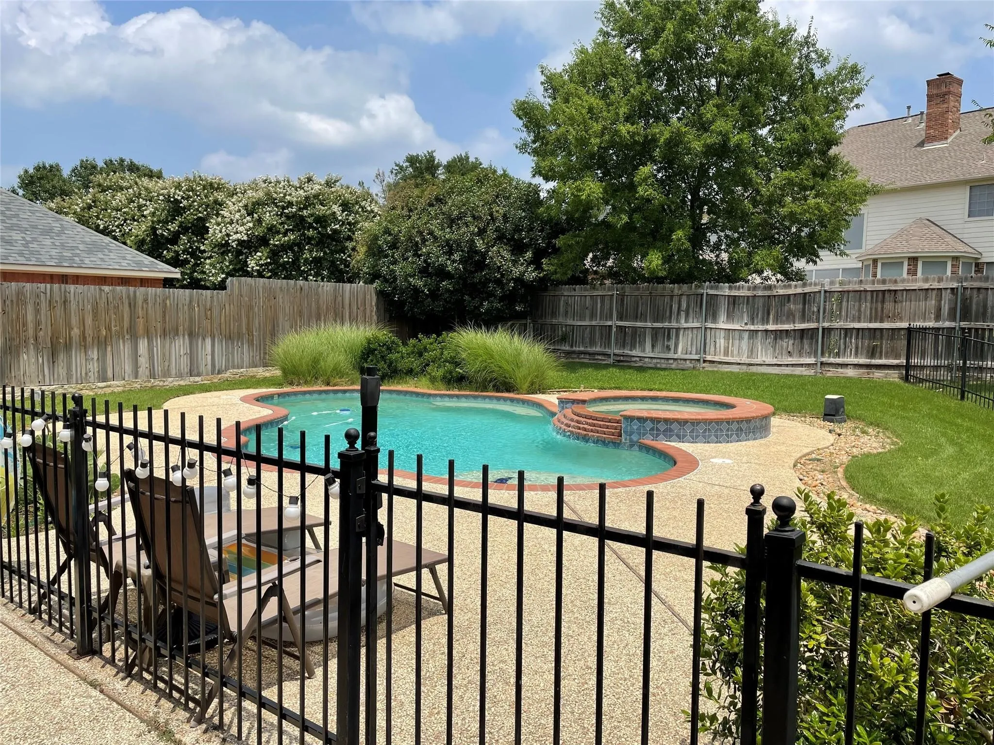 Outdoor pool with integrated spa, bordered by a concrete patio and a black metal fence