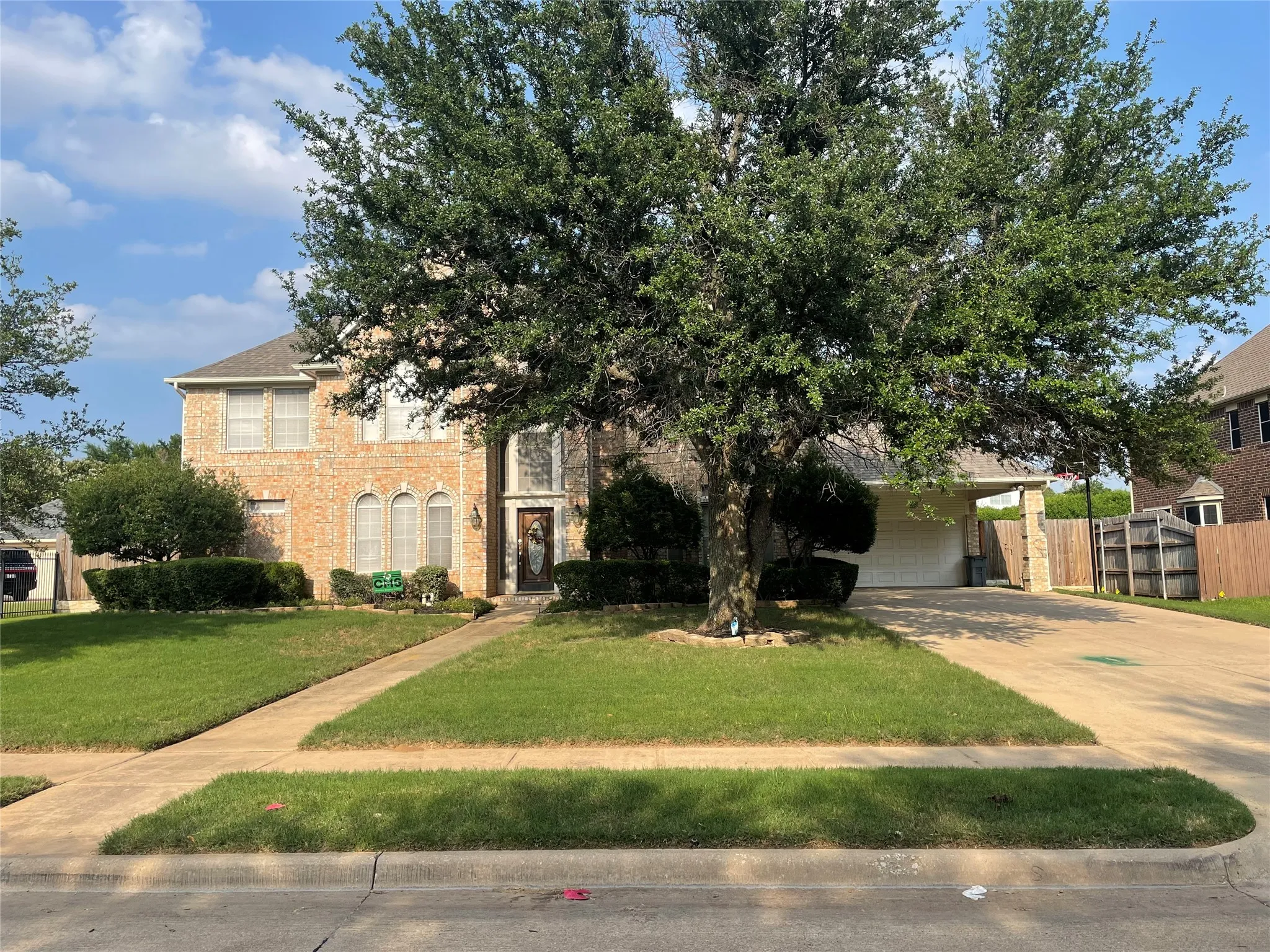 Brick facade residence with arched window details, a mature tree, and an attached garage