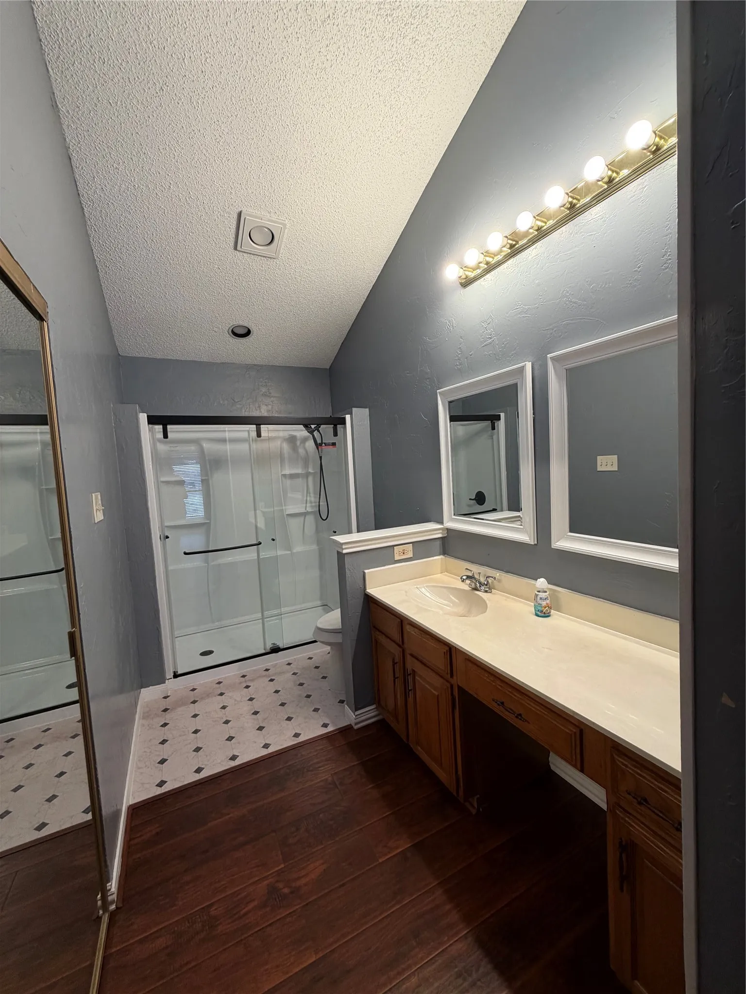 Spacious bathroom featuring a dual-sink vanity with wood-finish cabinetry, a large walk-in shower with sliding glass doors, and a combination of wood-finish and patterned tile flooring