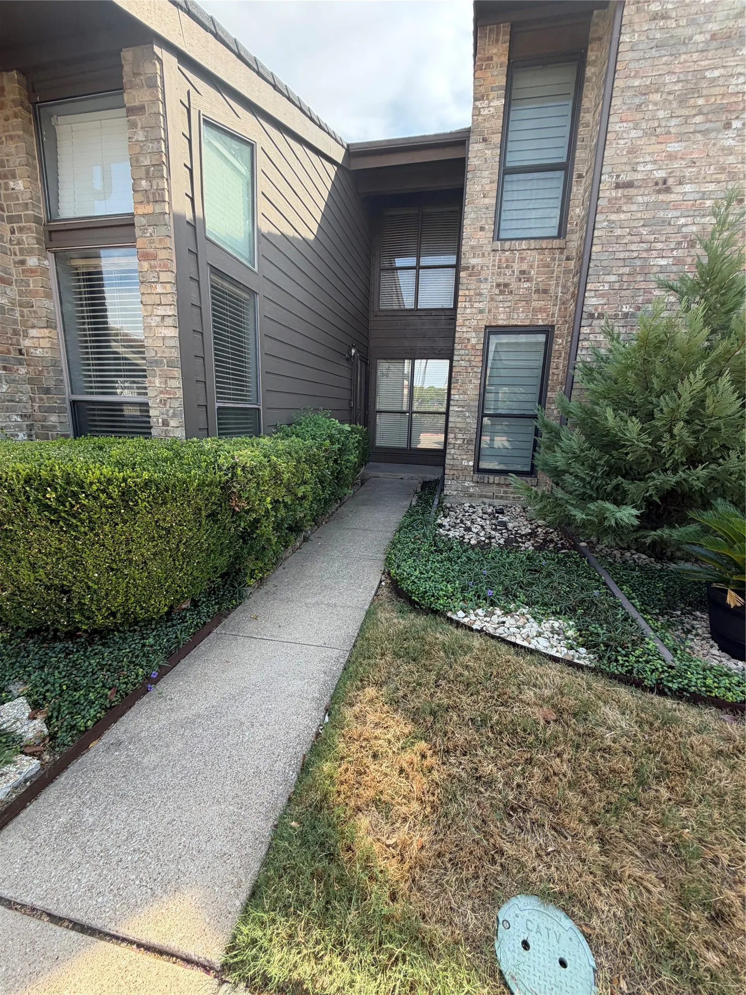 Brick and horizontal siding exterior with multiple window styles, concrete walkway, and established landscaping