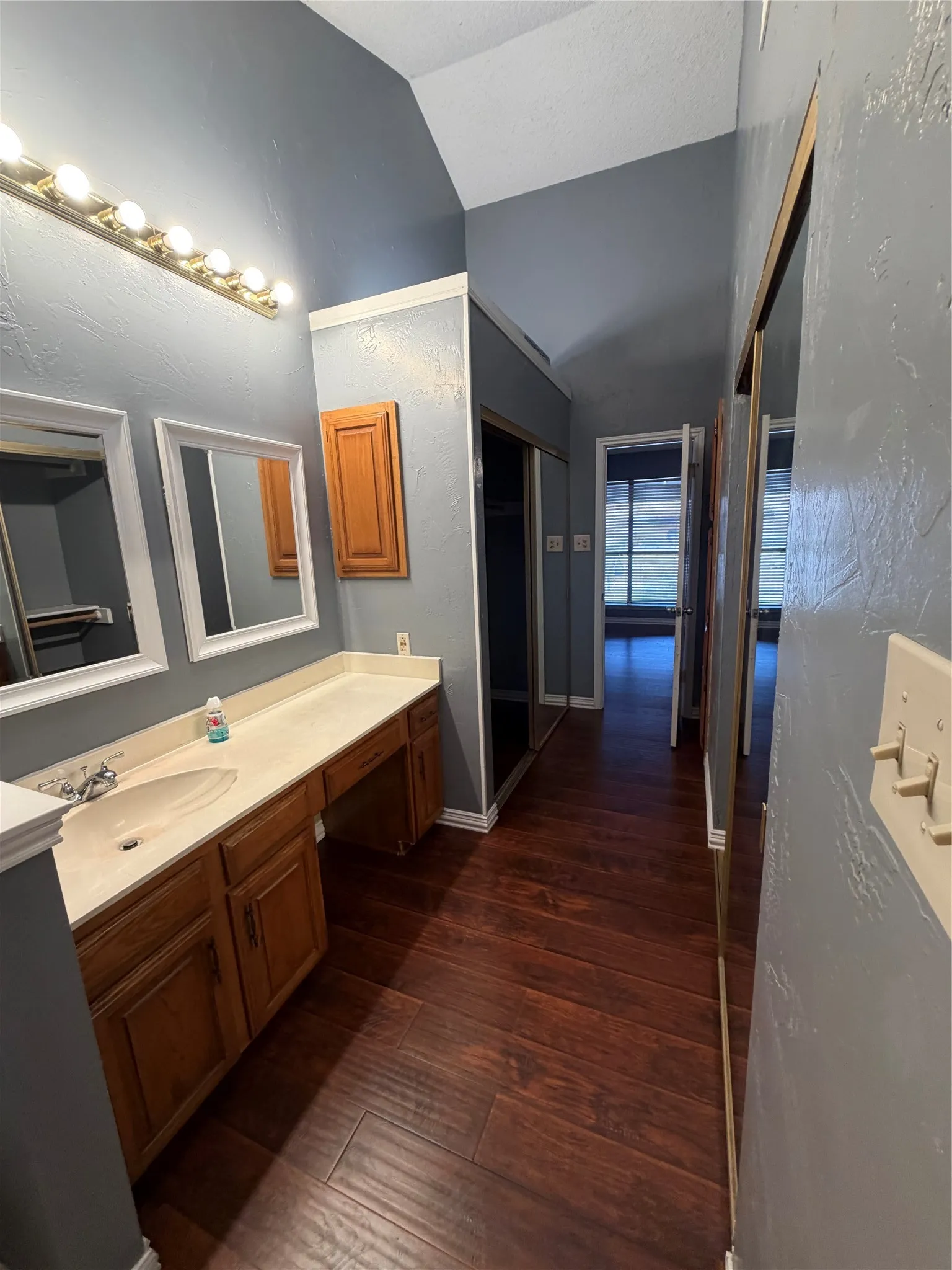 Vaulted ceiling with a vanity featuring a single basin sink, a wood-finish cabinet, and a wall-mounted light fixture