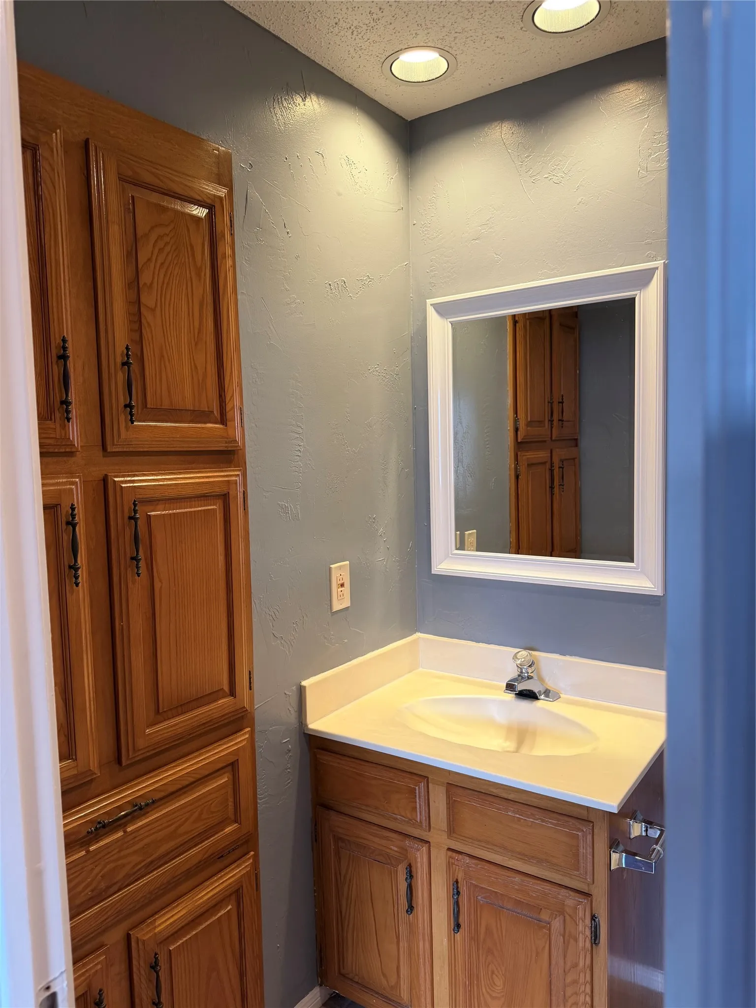 Recessed ceiling lighting, wood-finish cabinetry, built-in storage, vanity with integrated sink, and framed mirror