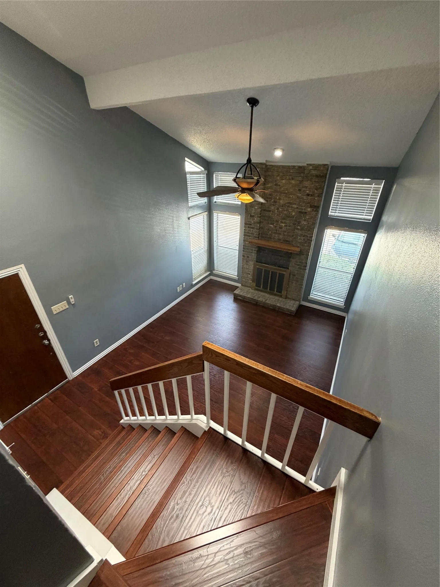 Vaulted ceiling with exposed beam, stone-clad fireplace, wood-finish flooring, and a contemporary ceiling fan