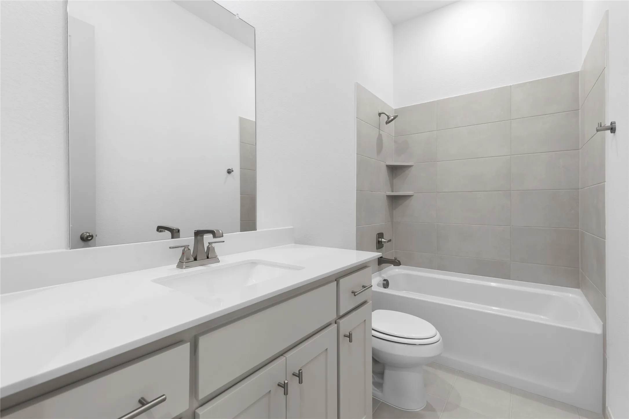 Modern bathroom featuring a single vanity with a white countertop and undermount sink, a large wall-mounted mirror, and a bathtub with tiled surround and built-in shelving