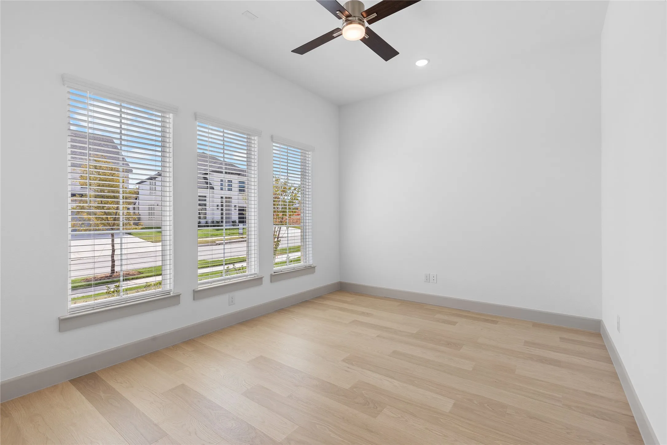 Light wood-finish flooring with crisp white walls, contemporary ceiling fan, recessed lighting, and three tall windows
