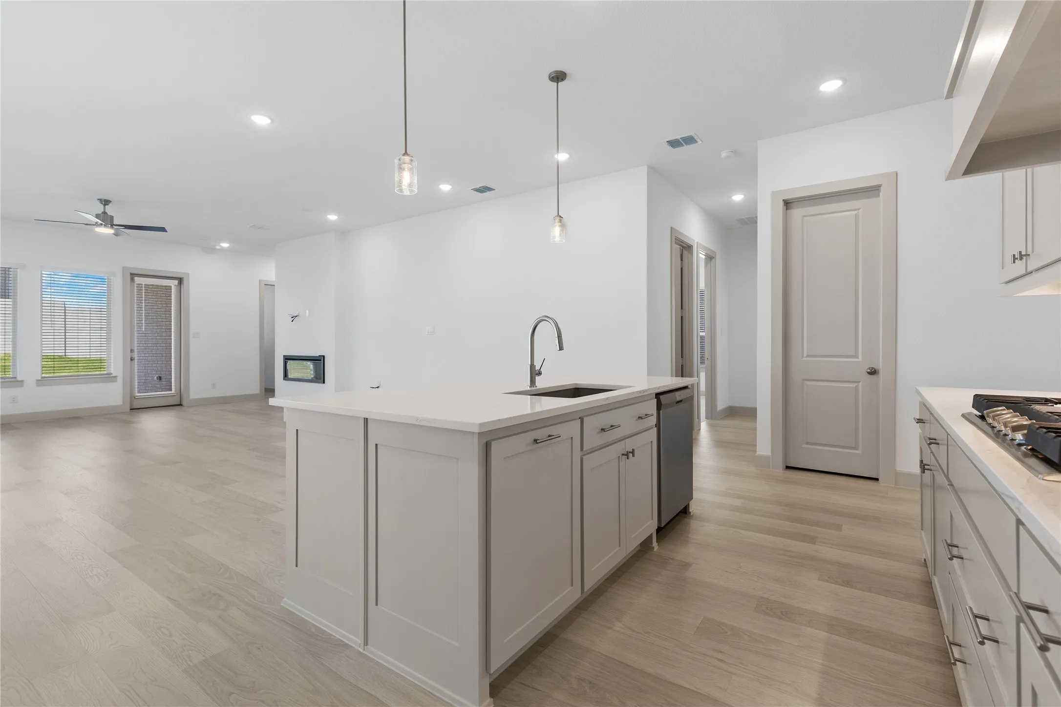 Kitchen island with integrated sink, stainless steel dishwasher, light wood-finish flooring, recessed lighting, and modern pendant lights