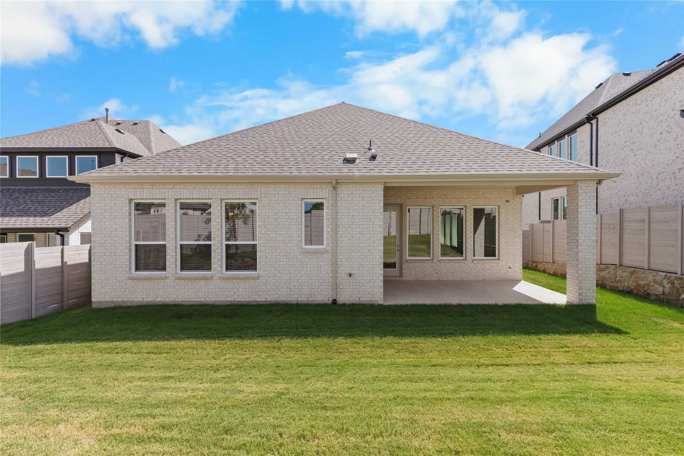 White brick exterior with a covered patio, multiple windows, and a shingle roof
