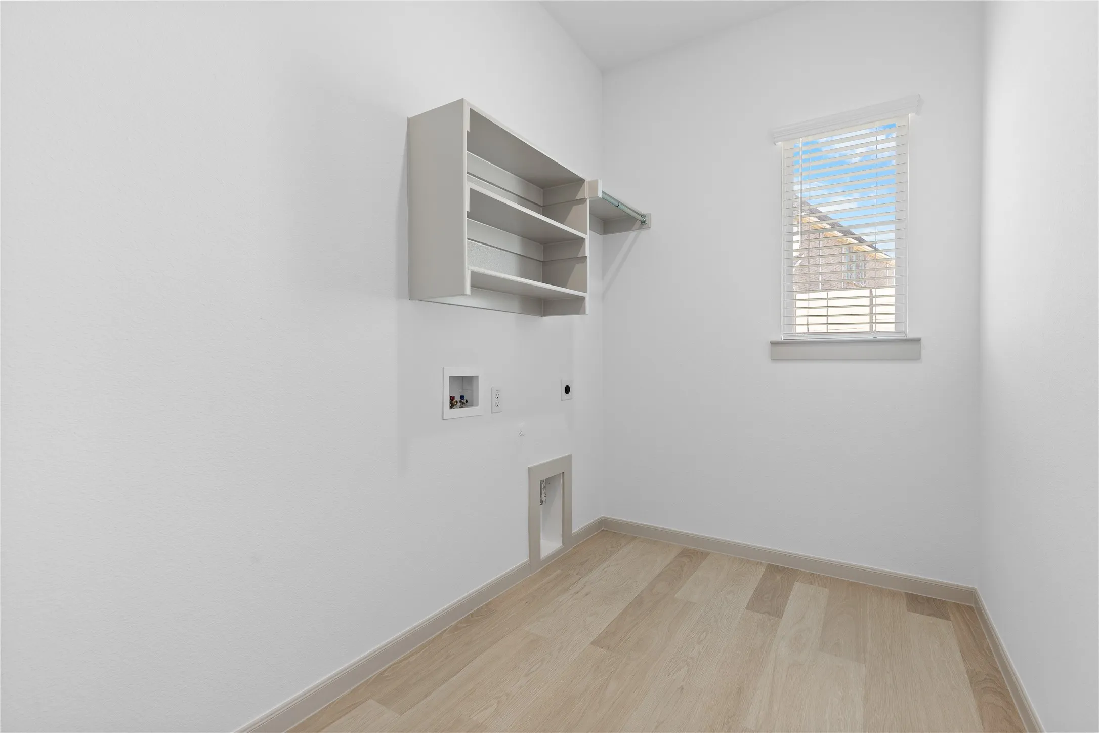 Dedicated utility area featuring wood-finish flooring, built-in shelving, and a window with blinds