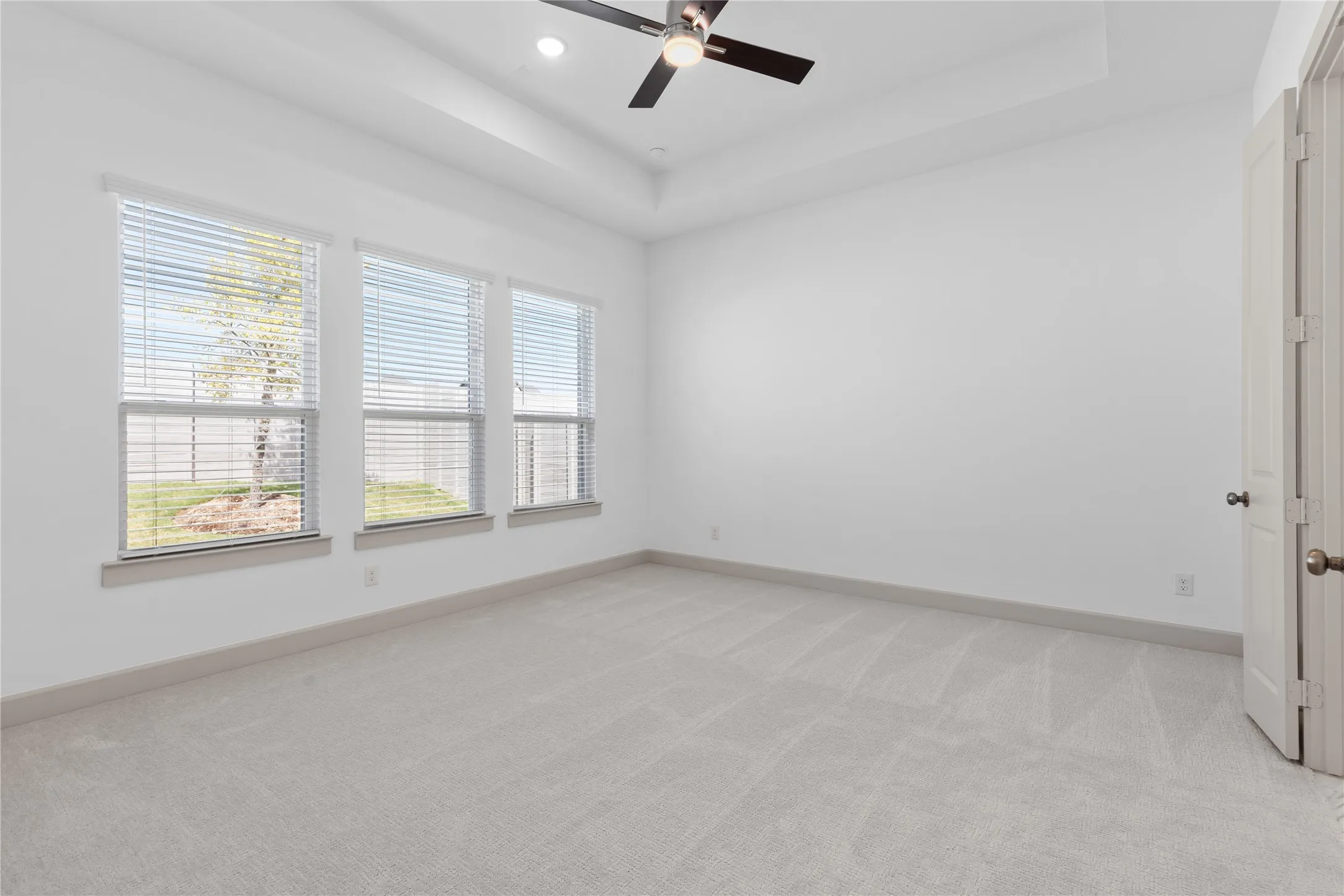 Tray ceiling with a ceiling fan, three windows with blinds, and light-toned carpeting