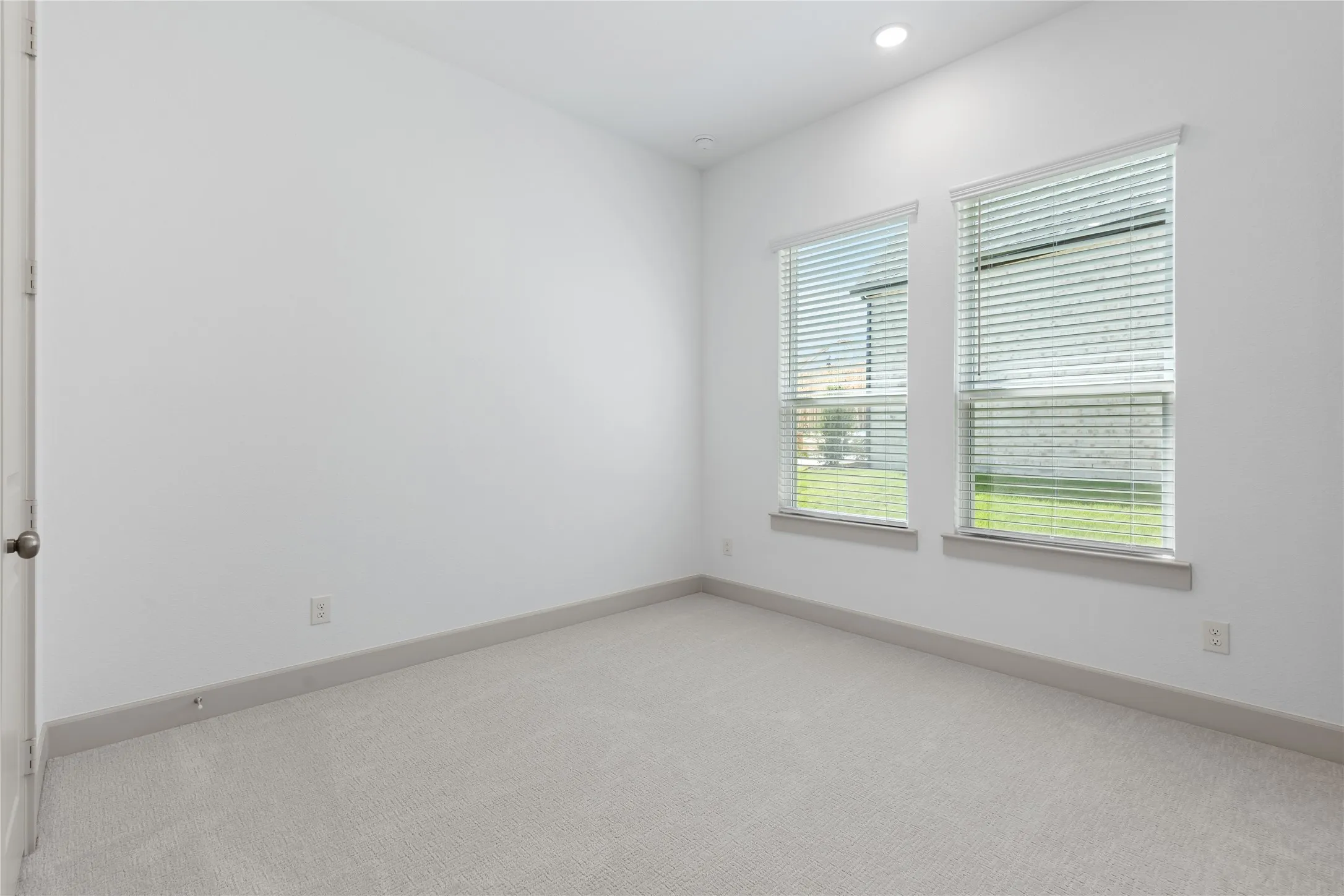 Recessed ceiling lighting, white painted walls, two windows with blinds, gray carpeting, and gray trim work