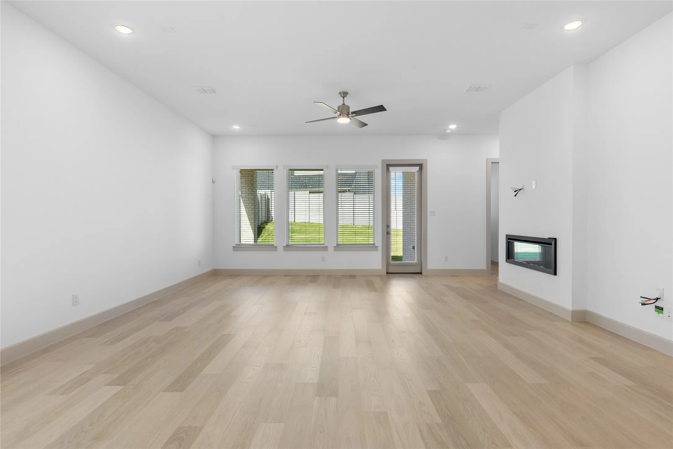 Spacious interior with light wood-finish flooring, recessed lighting, and a modern built-in fireplace