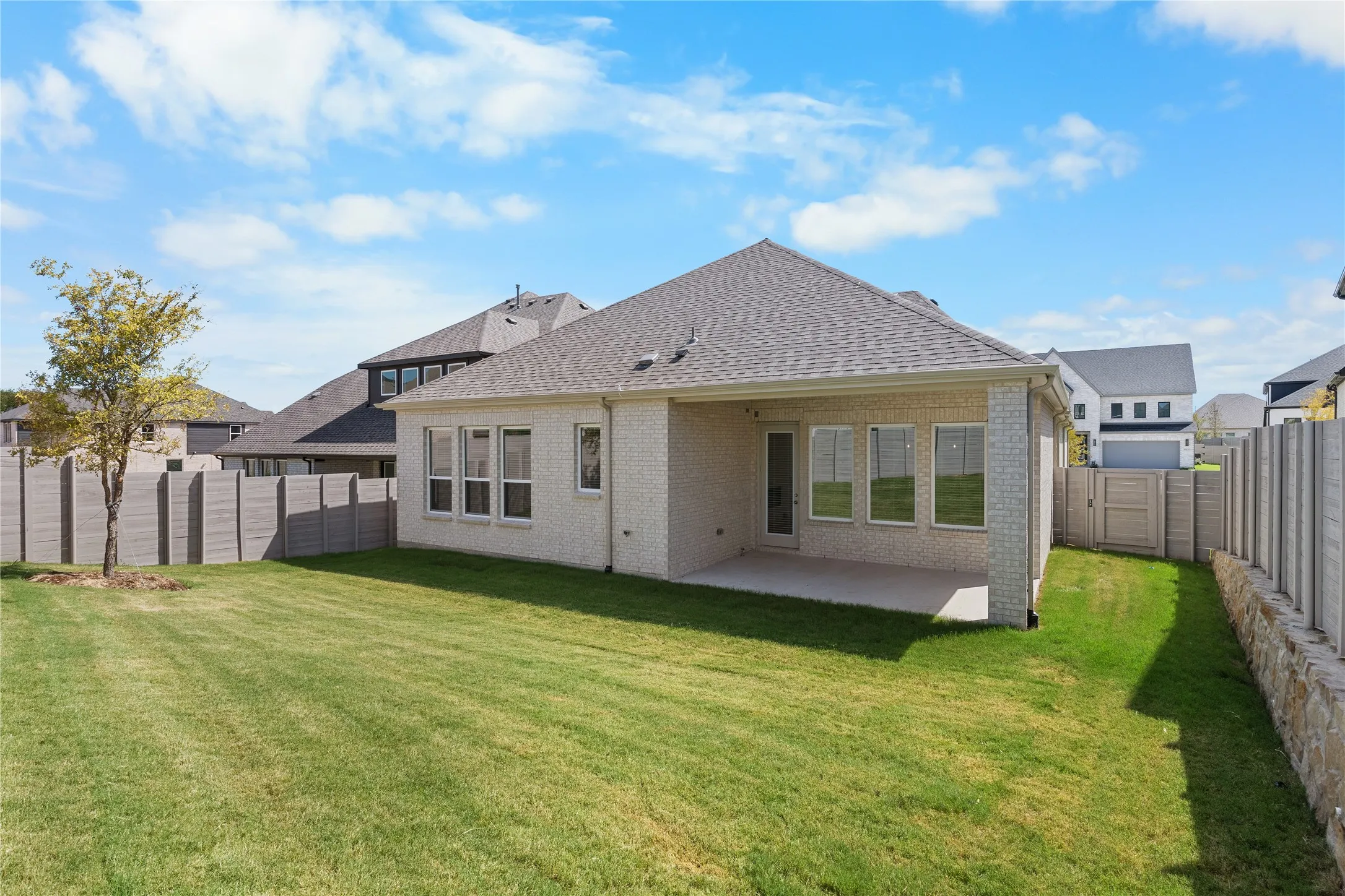 Expansive backyard featuring a large concrete patio, mature tree, and privacy fencing