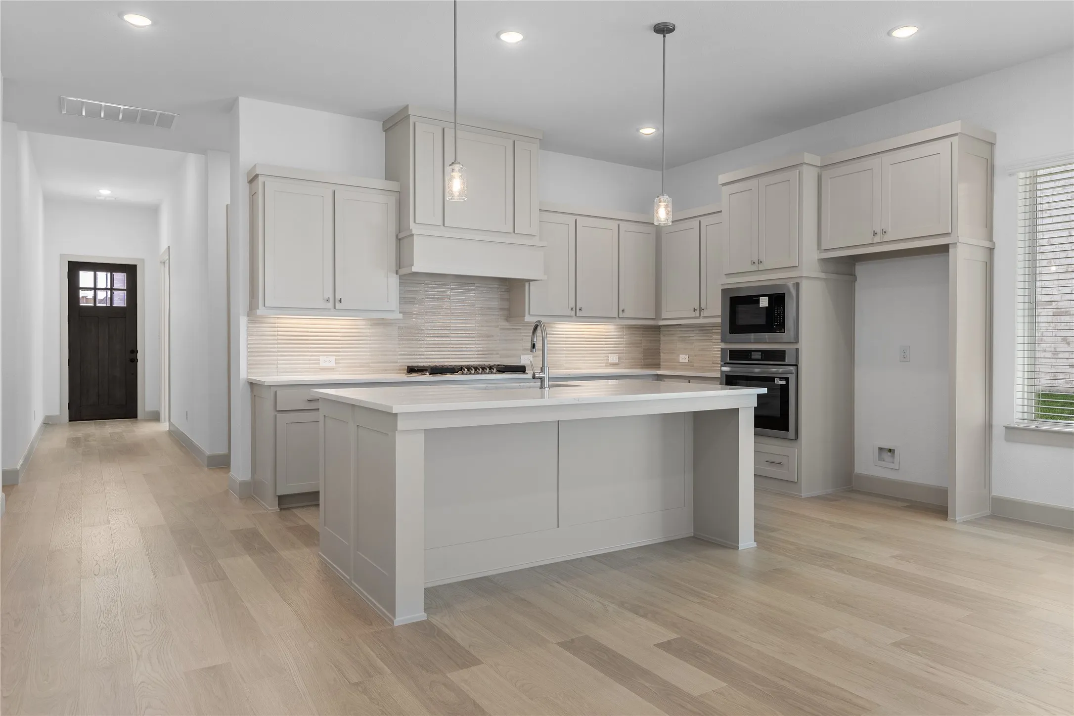 Gourmet kitchen with light-toned cabinetry, a spacious island, built-in stainless steel appliances, and wood-finish flooring