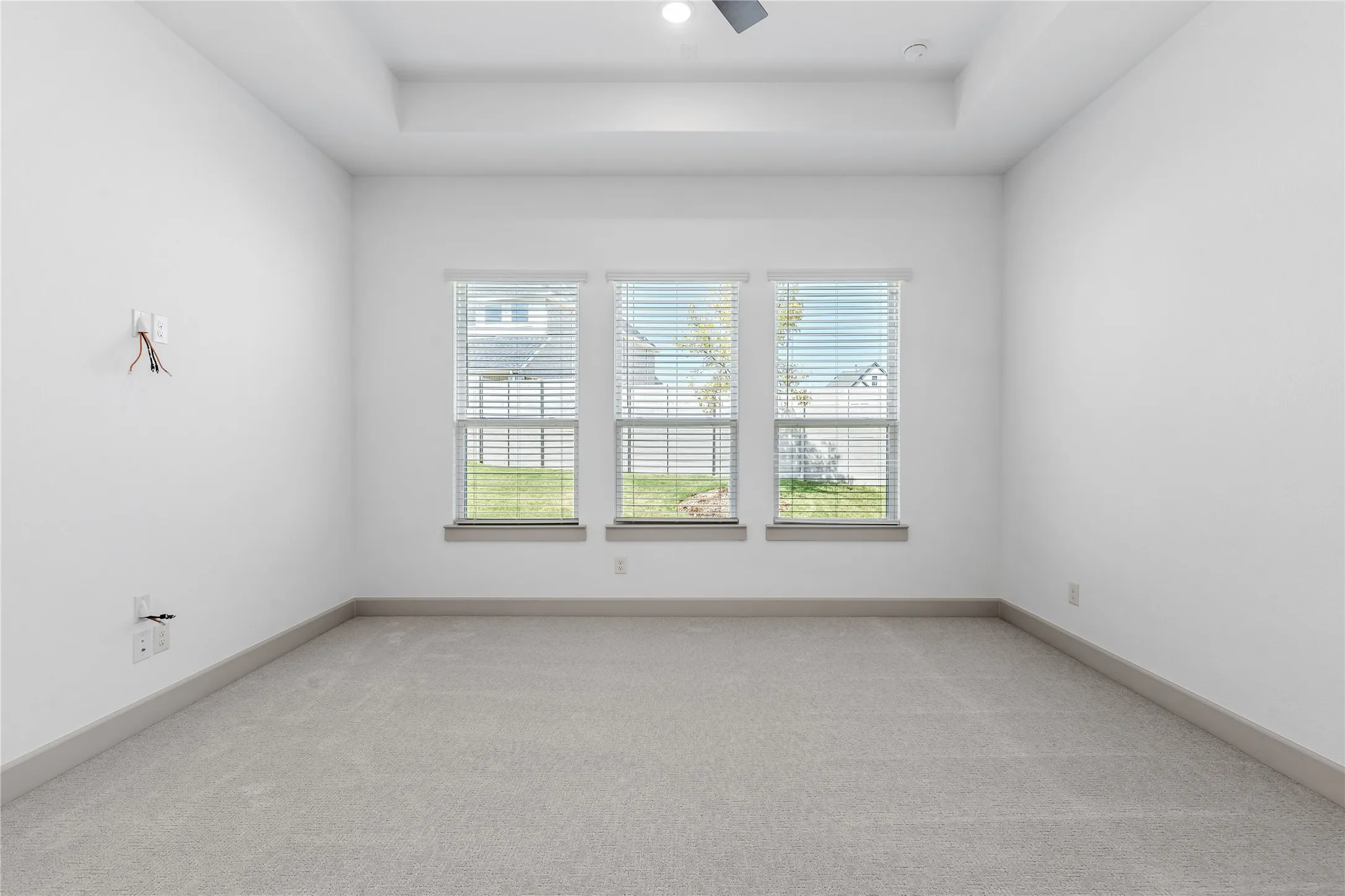 Recessed ceiling with a flush-mount light fixture, three large windows with horizontal blinds, neutral carpet flooring, and contemporary baseboards