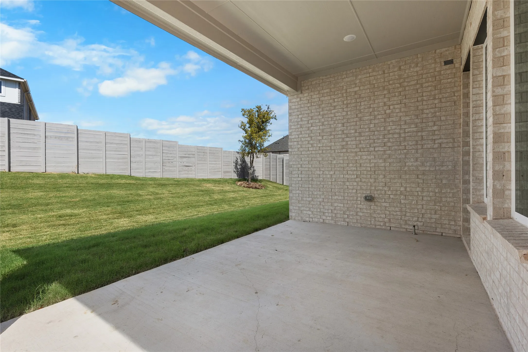Covered patio with a concrete surface, brick exterior, and a privacy fence