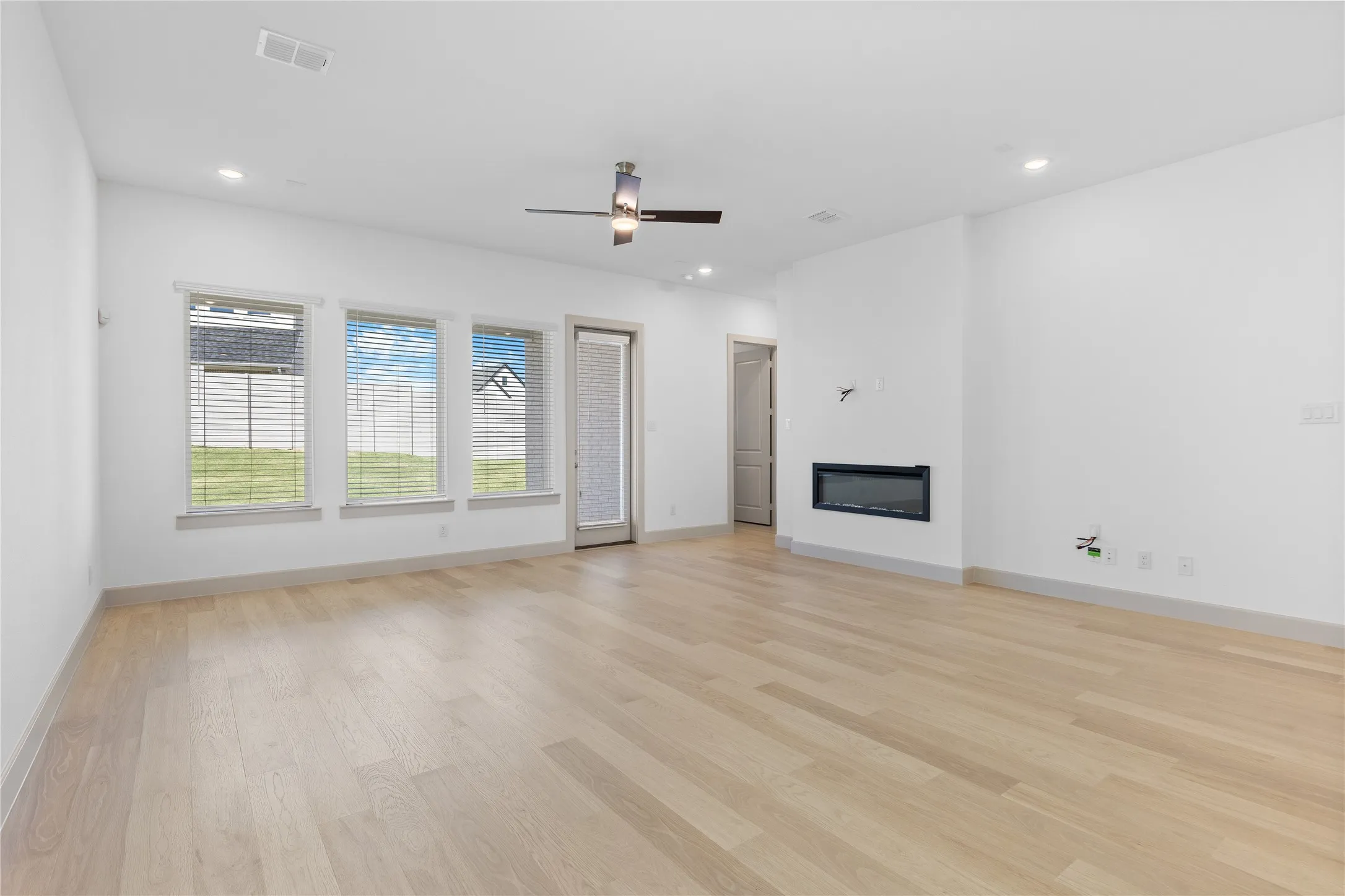 Wood-finish flooring, recessed lighting, ceiling fan, multiple windows, and a built-in electric fireplace