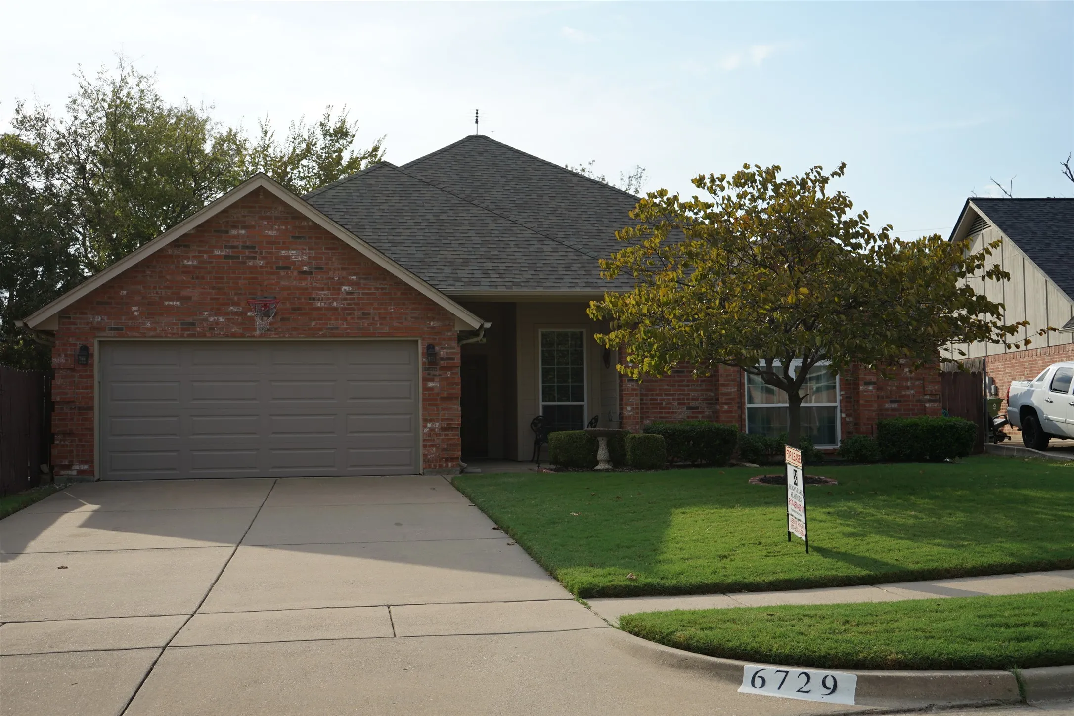 Brick facade, gray two-car garage, concrete driveway, front lawn, and mature tree