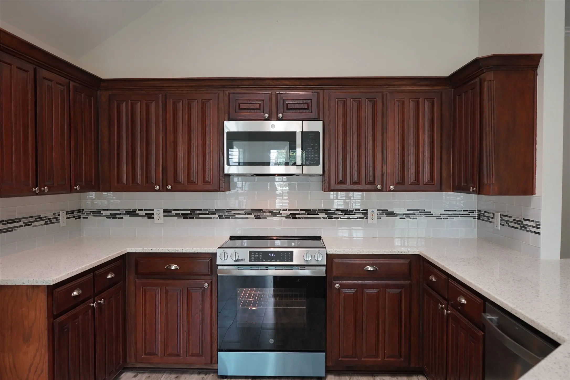 U-shaped kitchen featuring dark wood cabinetry, light-toned countertops, a full stainless steel range, a stainless steel microwave, and a white subway tile backsplash with decorative accents