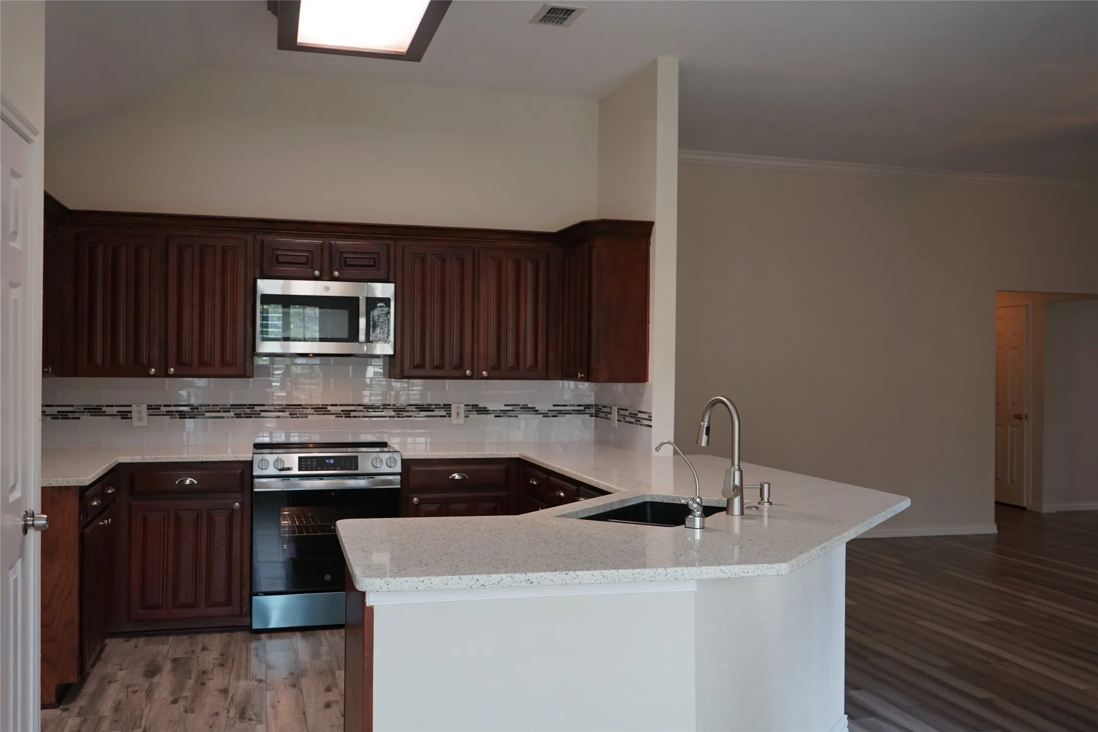Wood-finish flooring, dark wood cabinetry, white countertops, built-in stainless steel microwave, and a stainless steel range