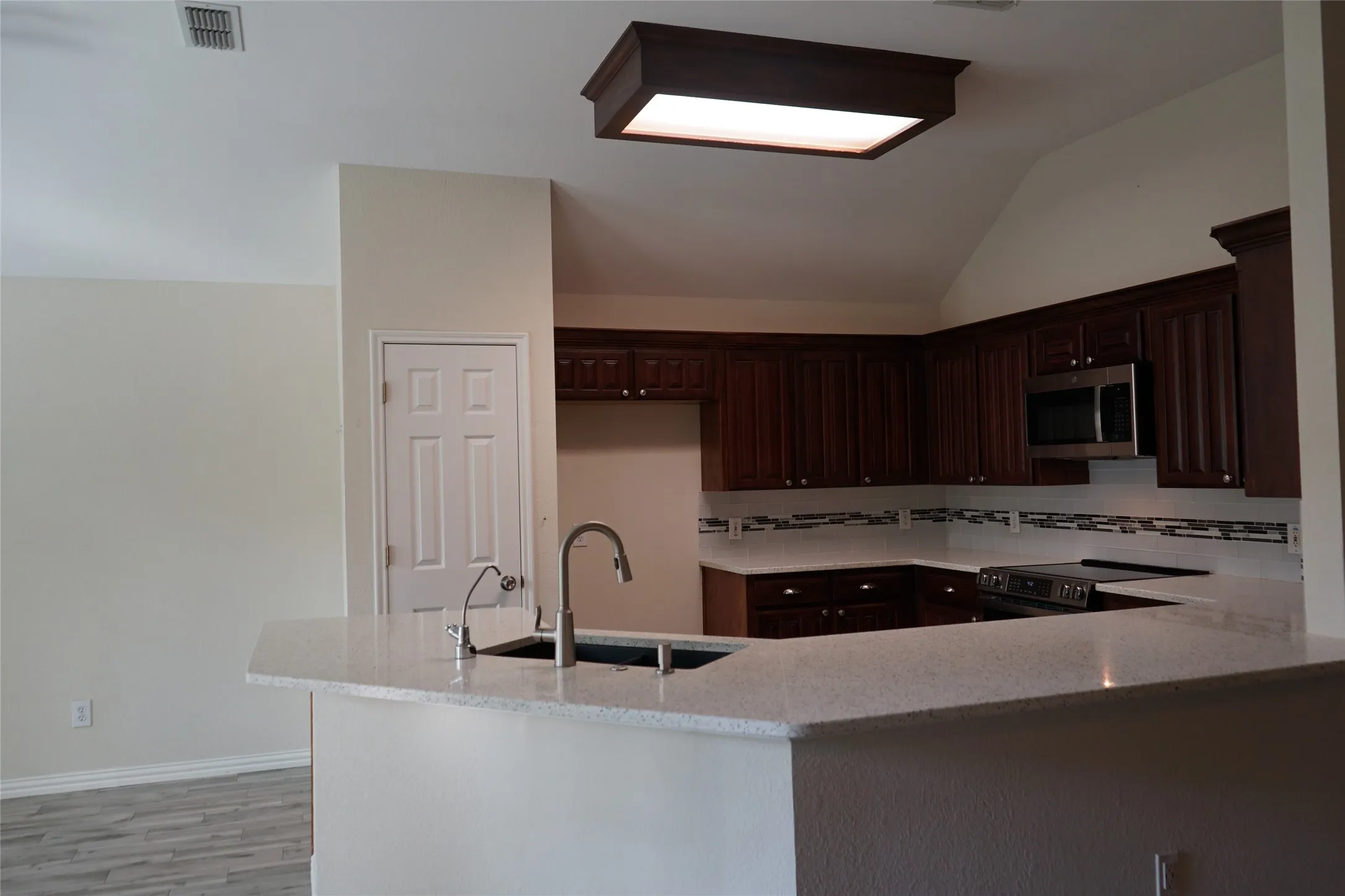 Kitchen featuring a breakfast bar with stone-finish countertops, stainless steel appliances, dark wood cabinetry, and a decorative tile backsplash