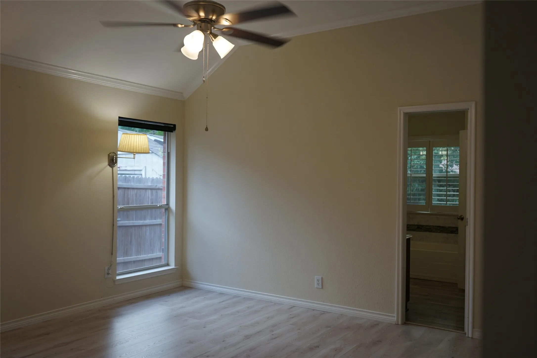 Vaulted ceiling with crown molding, wood-finish flooring, ceiling fan with integrated lighting, wall-mounted light fixture, and an interior doorway
