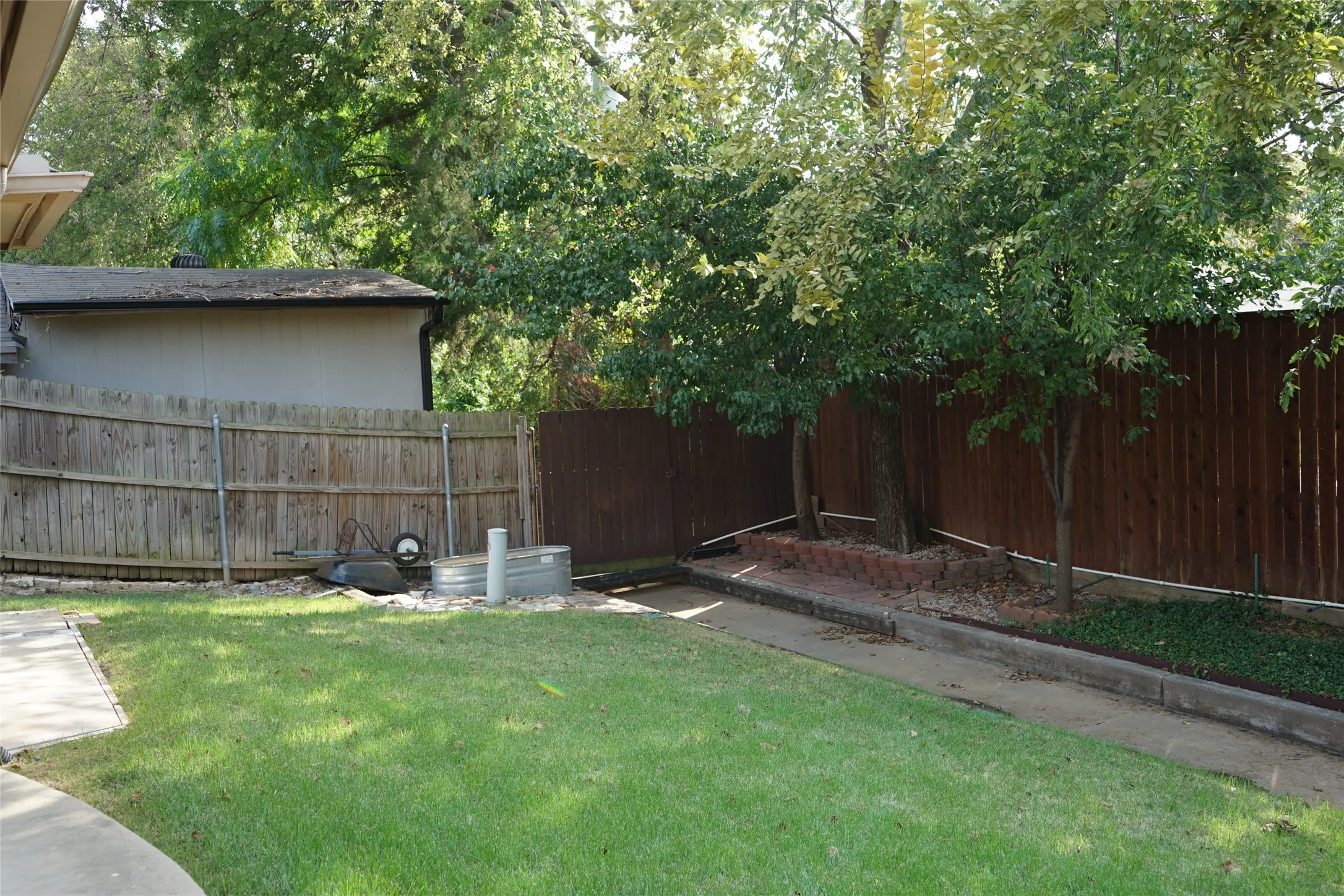Expansive grassy area featuring a concrete walkway, mature trees, and privacy fencing