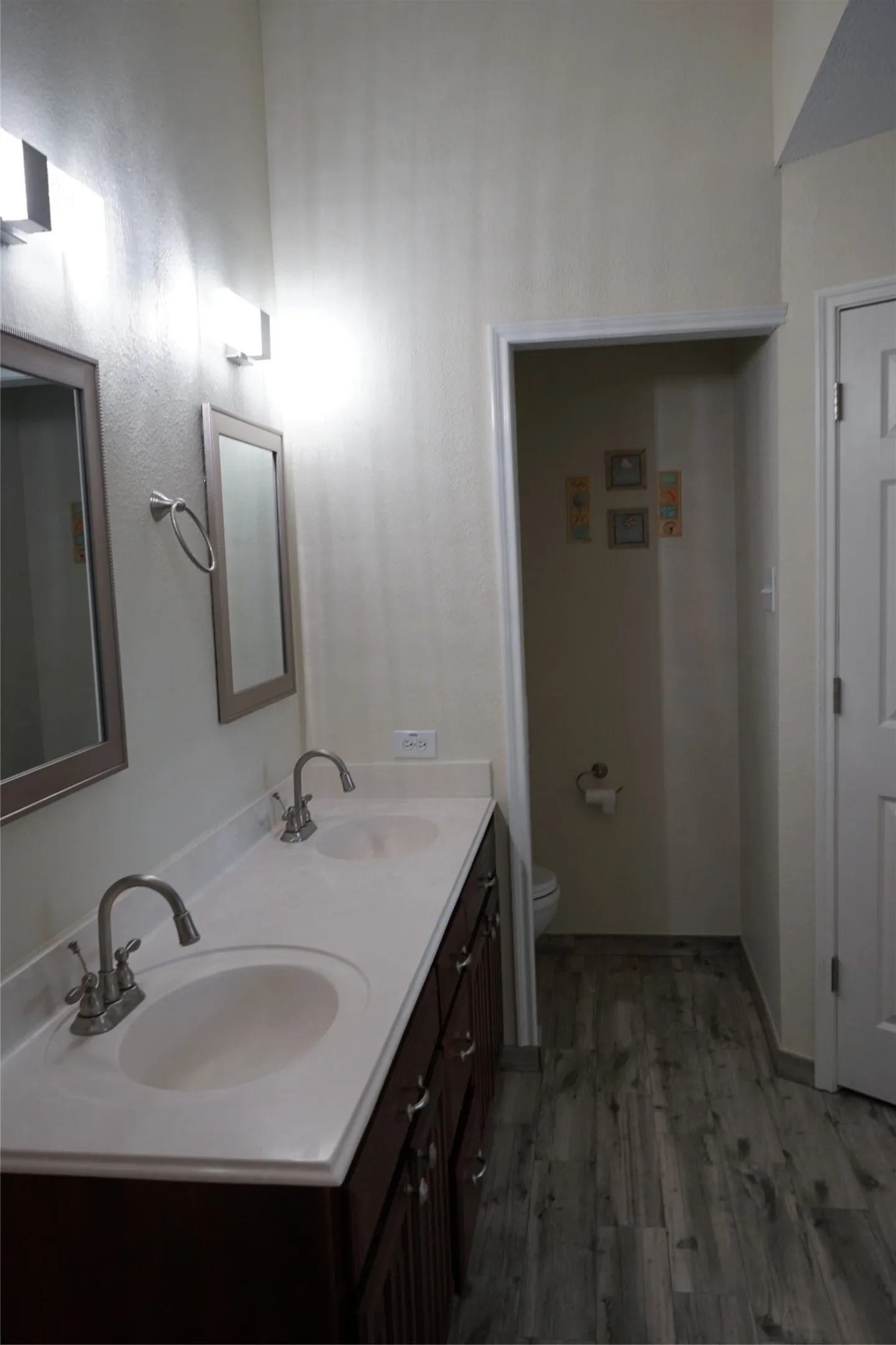 Dual vanity with an integrated countertop, dark wood-finish cabinetry, and wood-look plank flooring