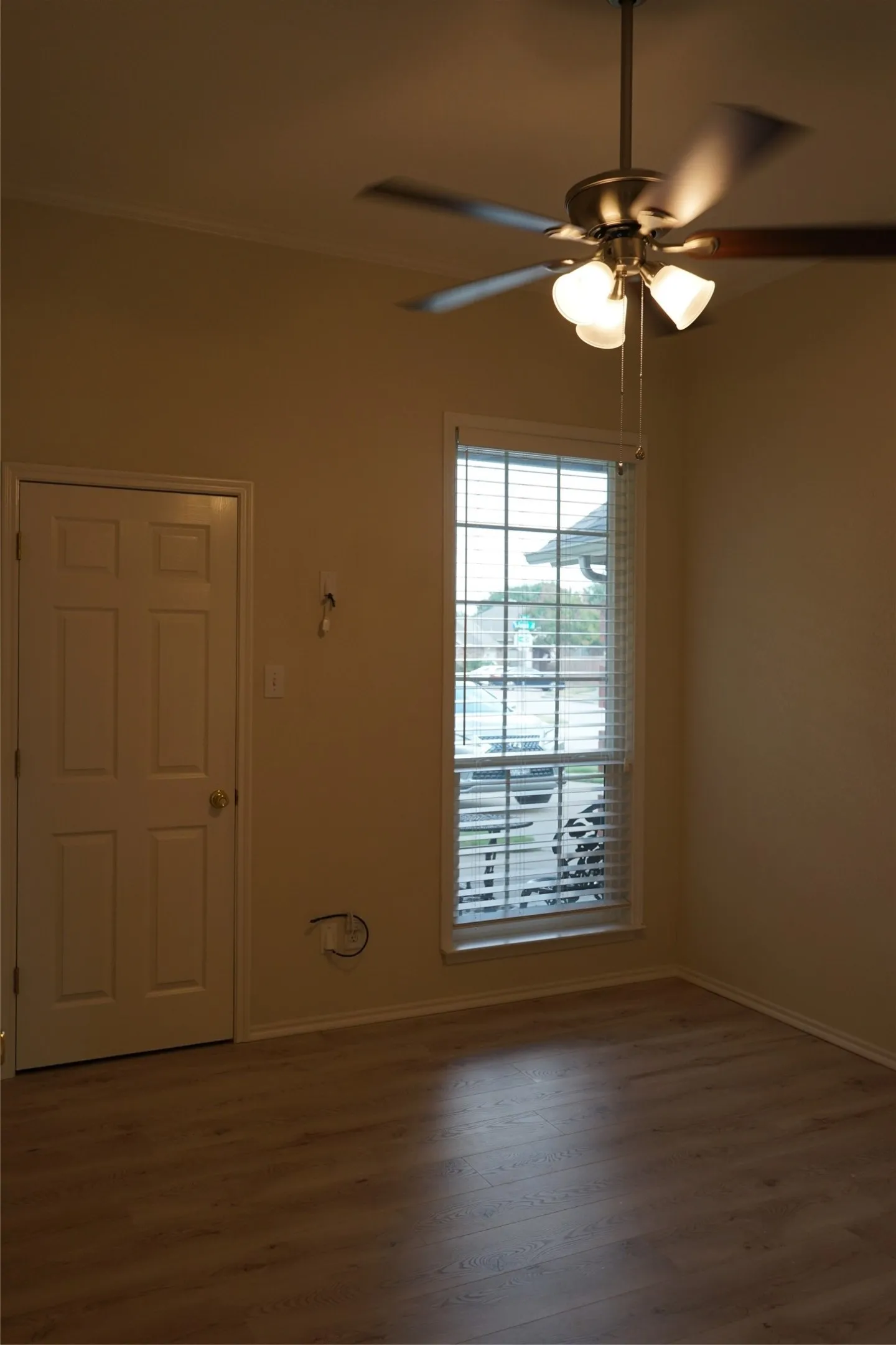 Wood-finish flooring with a ceiling fan light fixture, framed window with blinds, and a paneled door