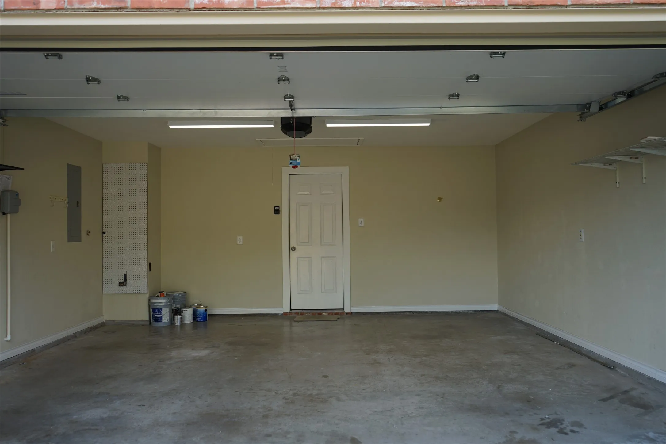 Spacious garage with light-toned walls, concrete flooring, overhead lighting, and built-in shelving