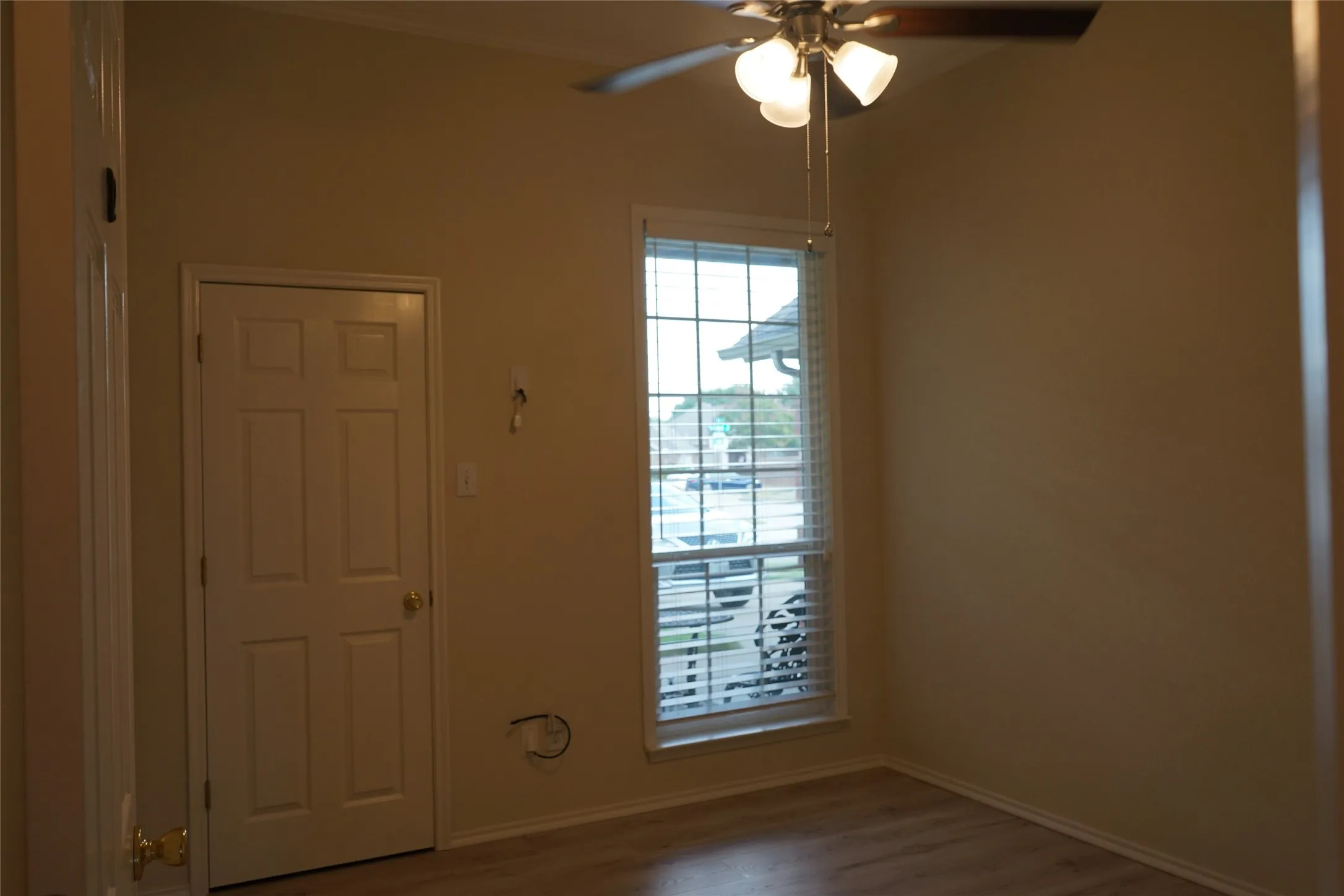Wood-finish flooring, ceiling fan with integrated lighting, window with horizontal blinds, six-panel interior door, and neutral wall tones