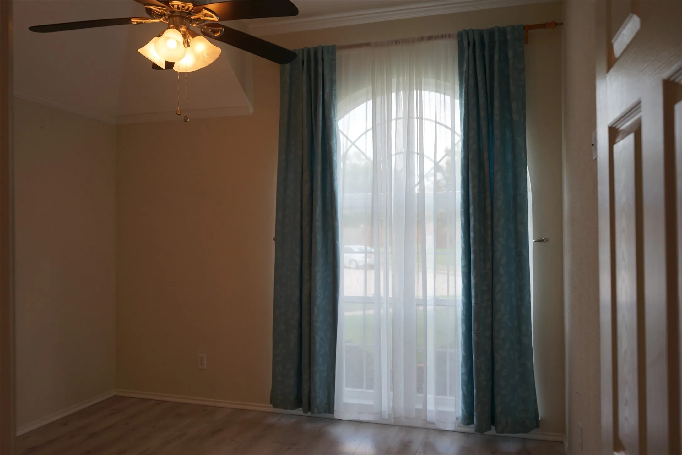 Arched window with decorative grilles, wood-finish flooring, ceiling fan with integrated lighting, and crown molding