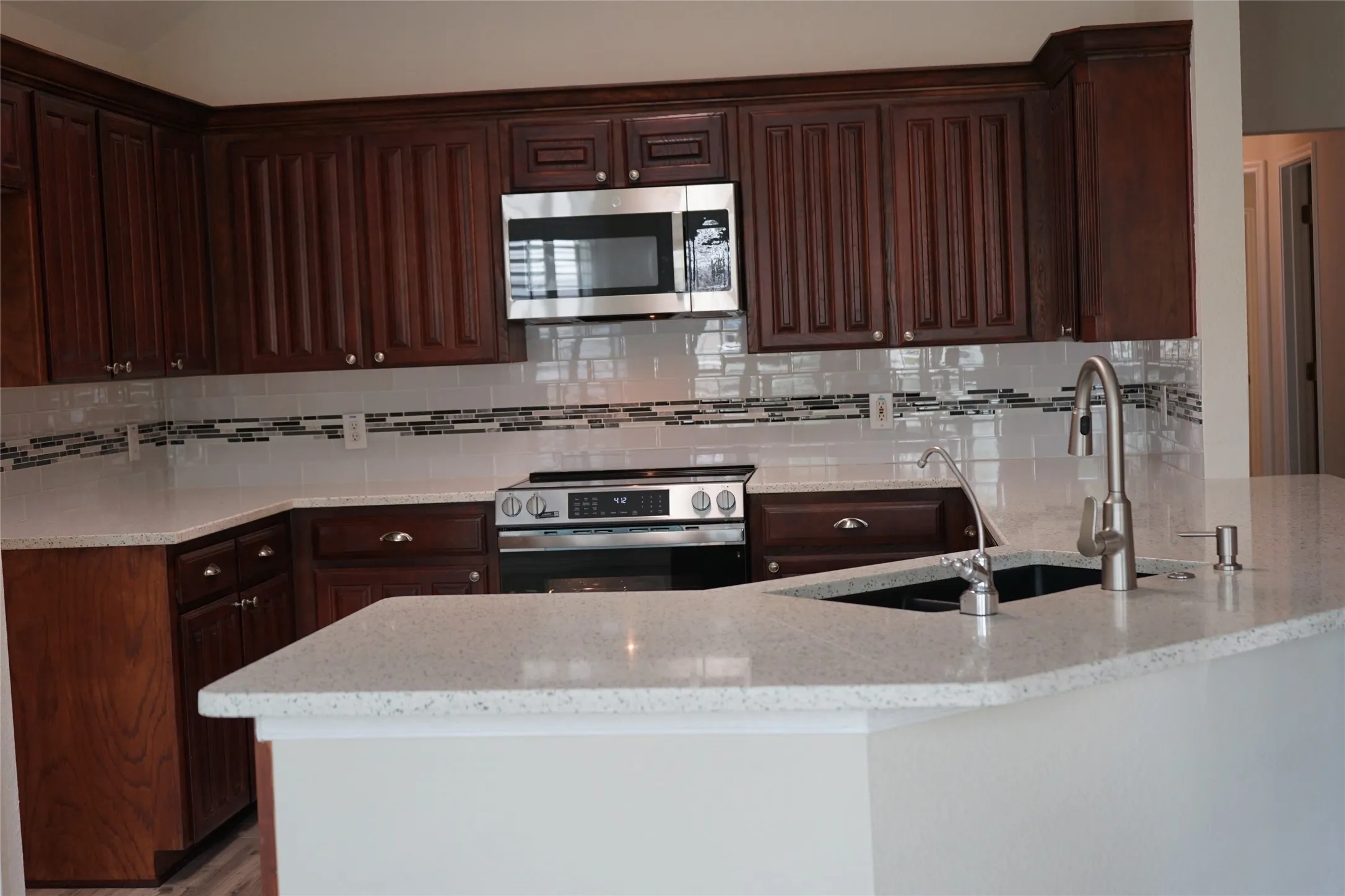 Kitchen featuring cherry-finish cabinetry, light-toned countertops, a stainless steel microwave, a stainless steel range, and a tile backsplash with decorative accent banding