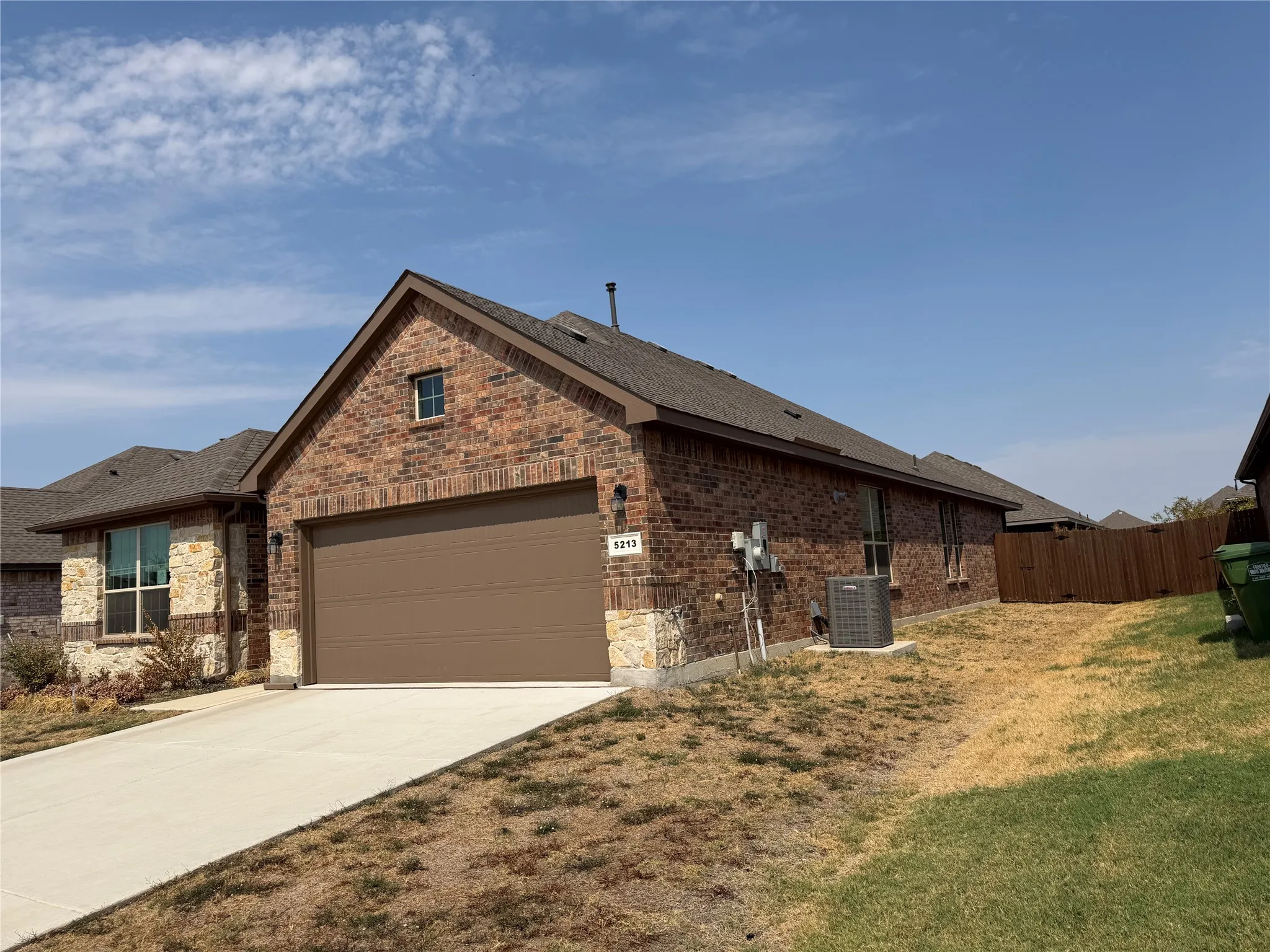 Brick and stone exterior with a brown garage door, concrete driveway, and gabled roofline