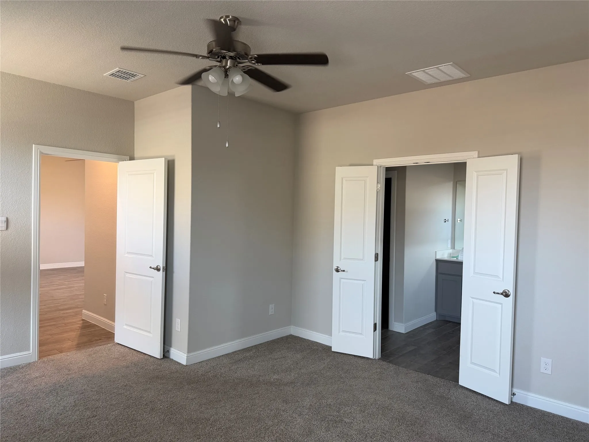 Carpeted flooring, neutral wall tones, ceiling fan with integrated lighting, white paneled doors, and wood-look flooring visible through doorways